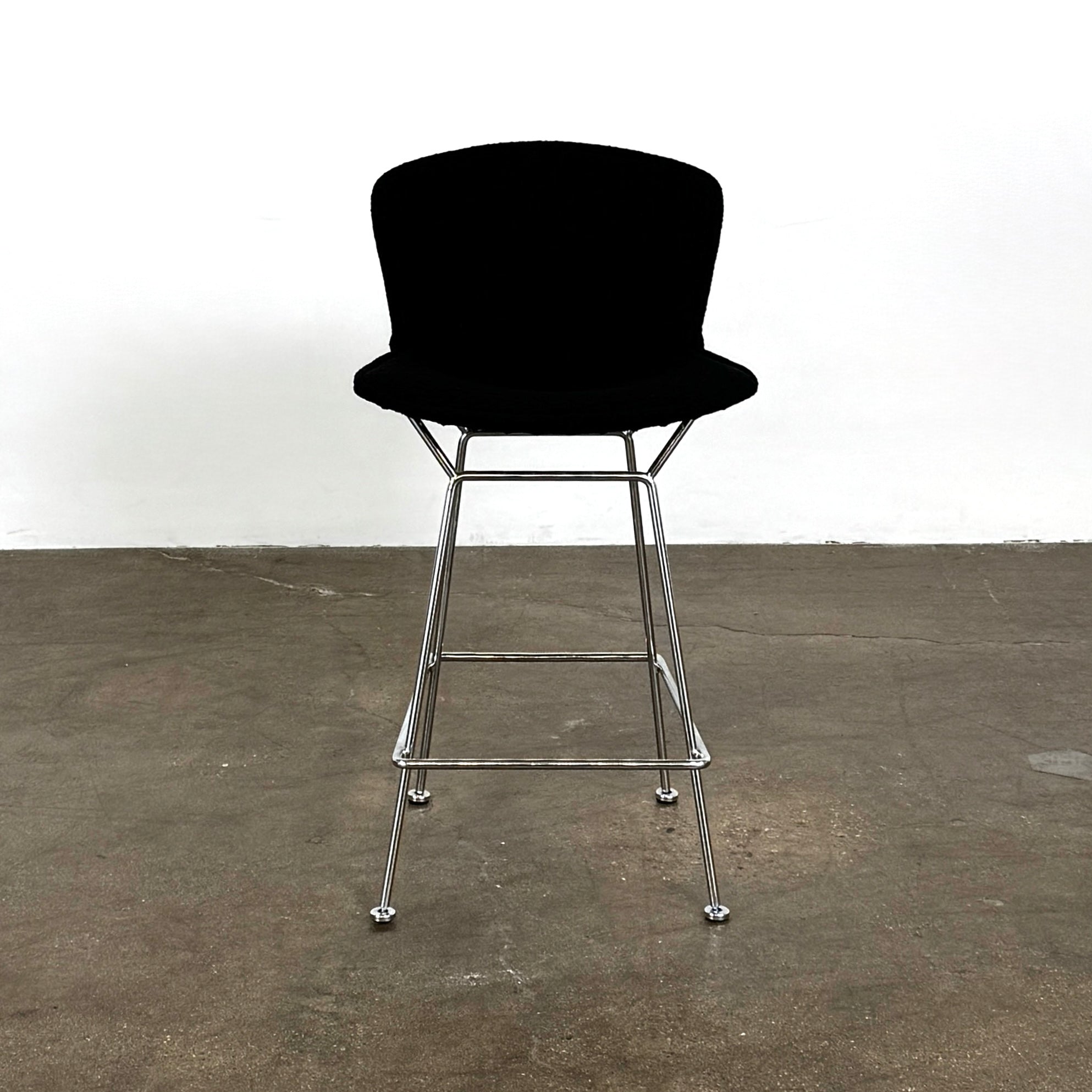 Close-up of a Knoll Bertoia Counter Stool from a set of 4, featuring a black cushion and textured black fabric over the backrest, placed on a polished concrete floor.