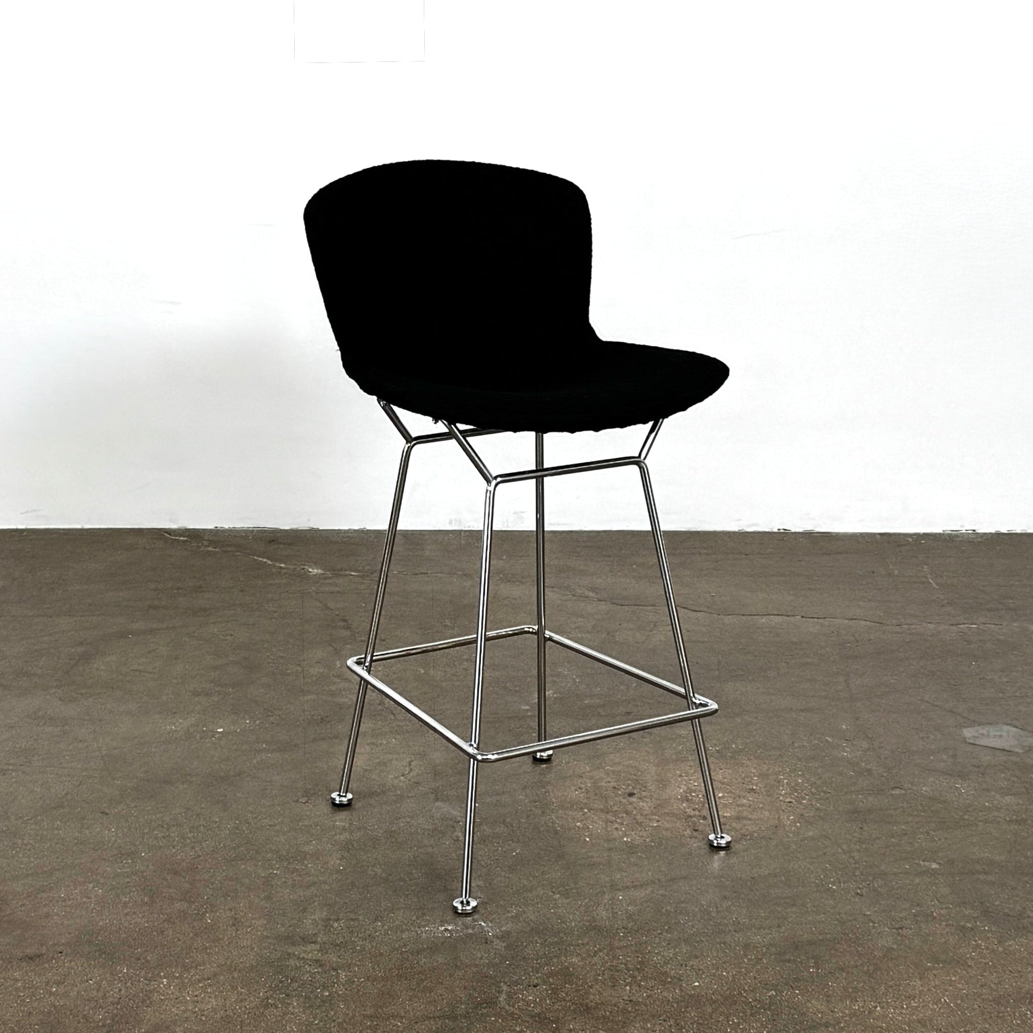 Close-up of a Knoll Bertoia Counter Stool from a set of 4, featuring a black cushion and textured black fabric over the backrest, placed on a polished concrete floor.