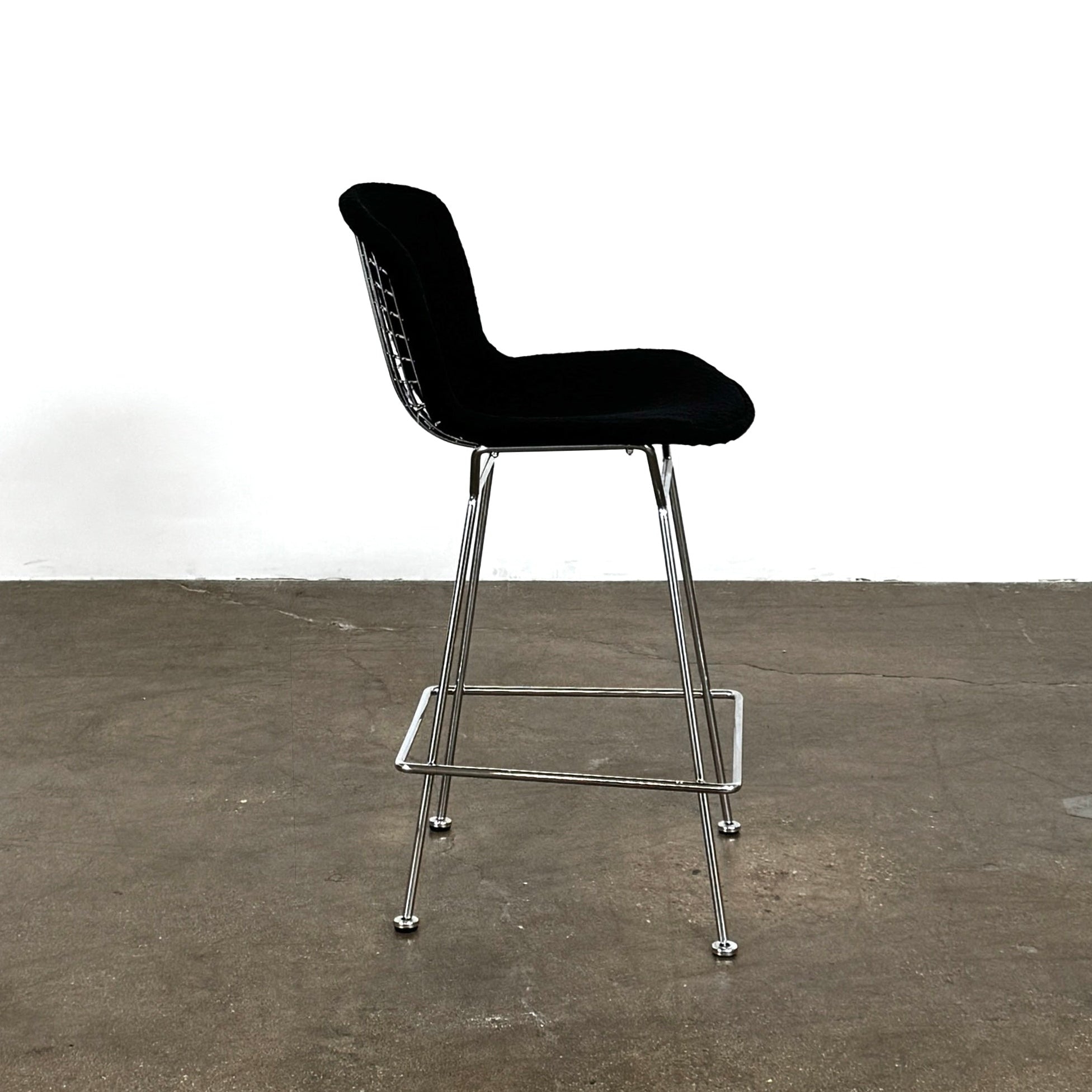 Close-up of a Knoll Bertoia Counter Stool from a set of 4, featuring a black cushion and textured black fabric over the backrest, placed on a polished concrete floor.