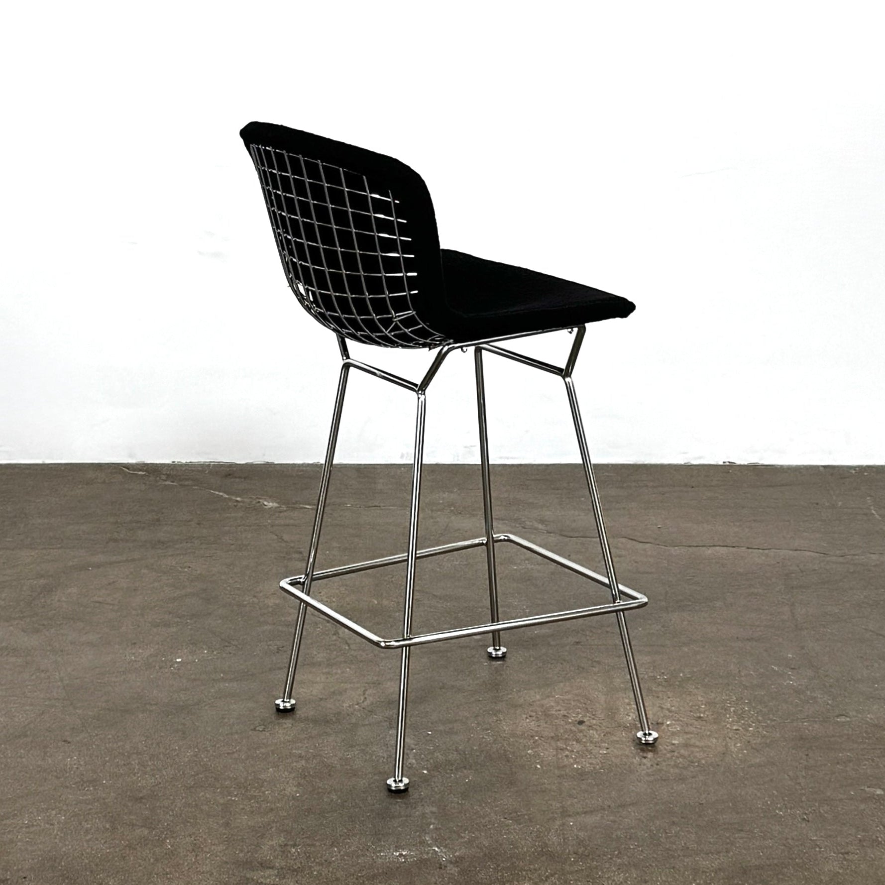 Close-up of a Knoll Bertoia Counter Stool from a set of 4, featuring a black cushion and textured black fabric over the backrest, placed on a polished concrete floor.
