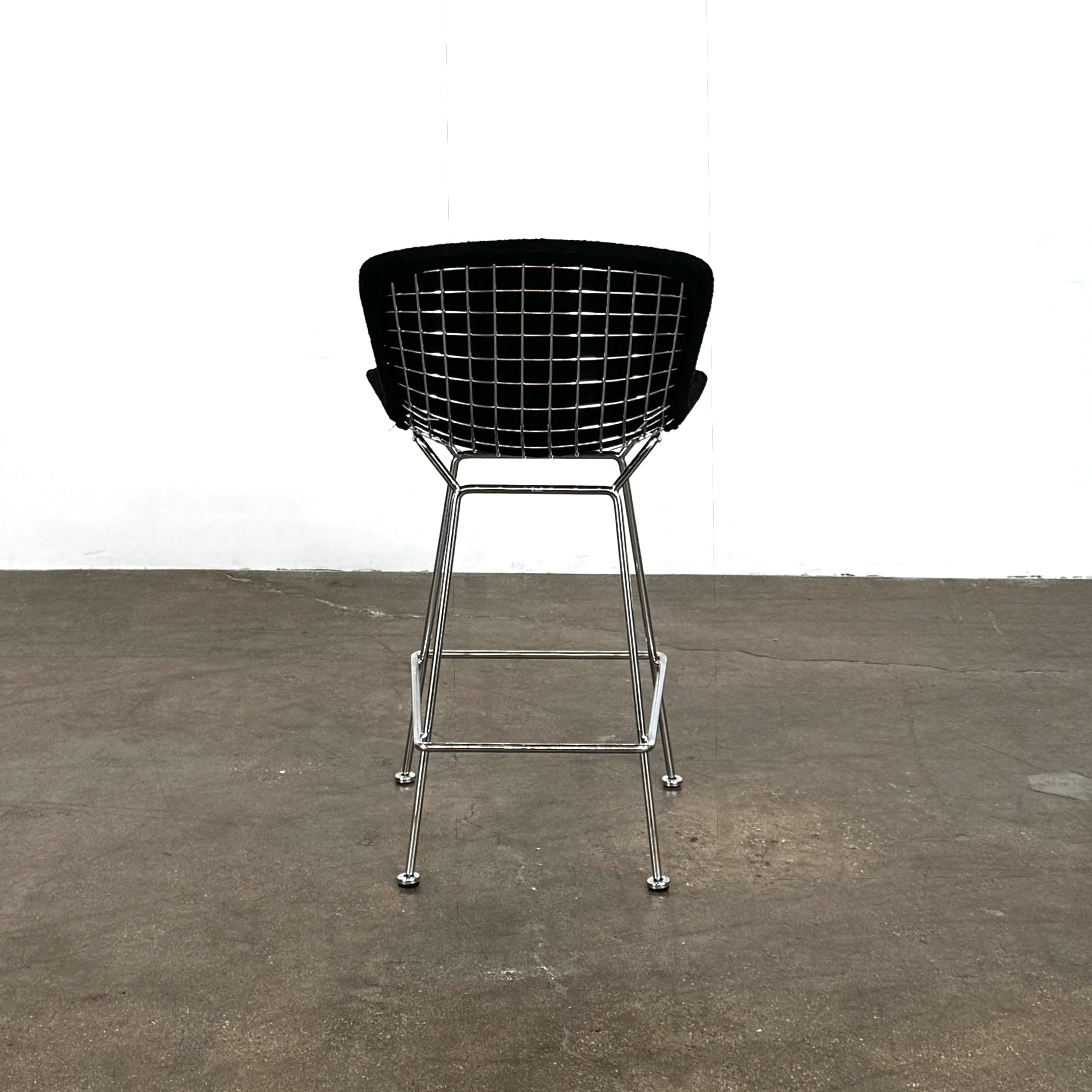 Close-up of a Knoll Bertoia Counter Stool from a set of 4, featuring a black cushion and textured black fabric over the backrest, placed on a polished concrete floor.