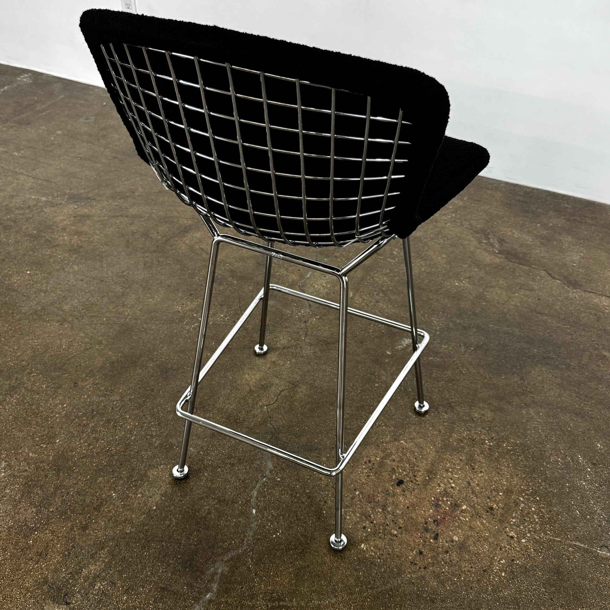 Close-up of a Knoll Bertoia Counter Stool from a set of 4, featuring a black cushion and textured black fabric over the backrest, placed on a polished concrete floor.