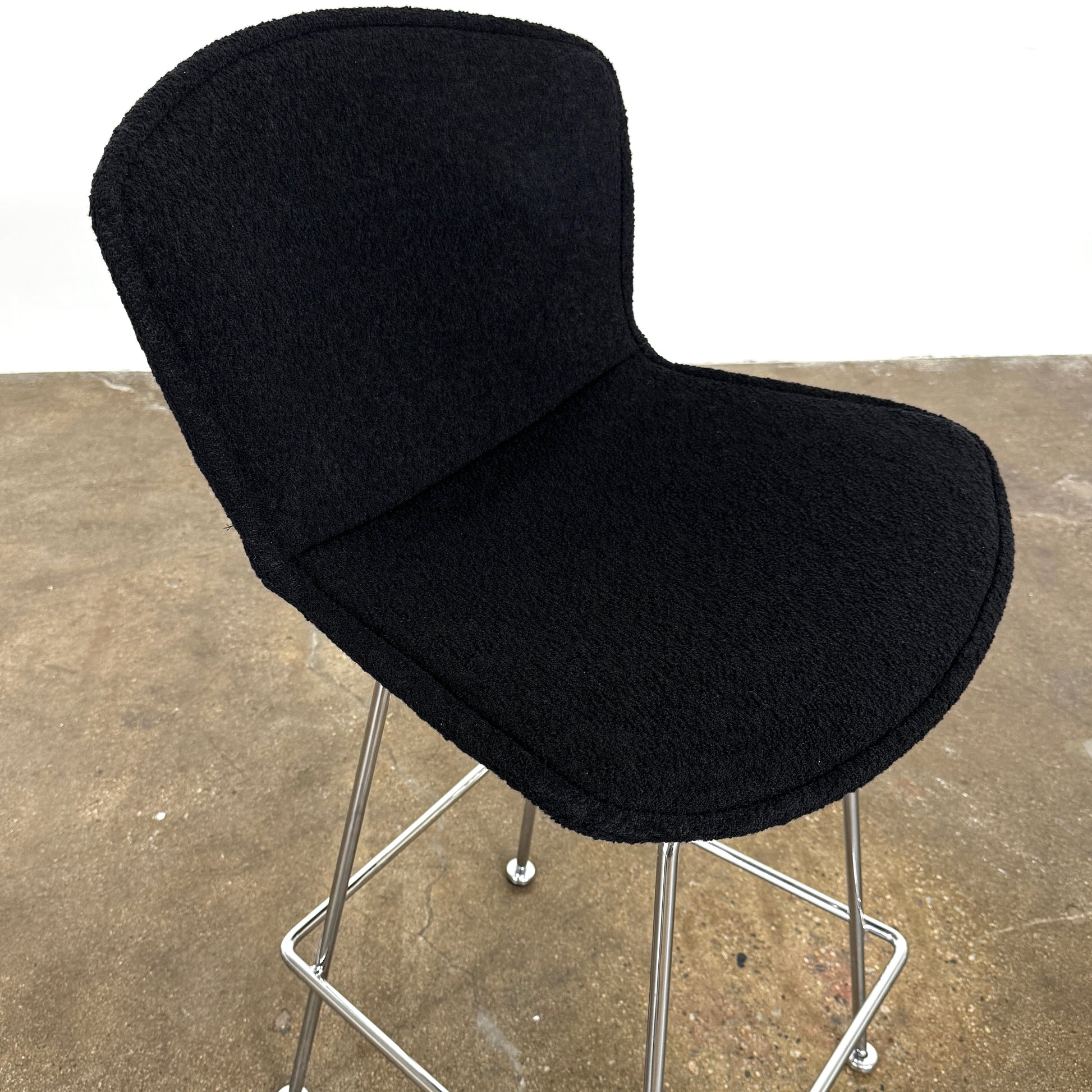 Close-up of a Knoll Bertoia Counter Stool from a set of 4, featuring a black cushion and textured black fabric over the backrest, placed on a polished concrete floor.
