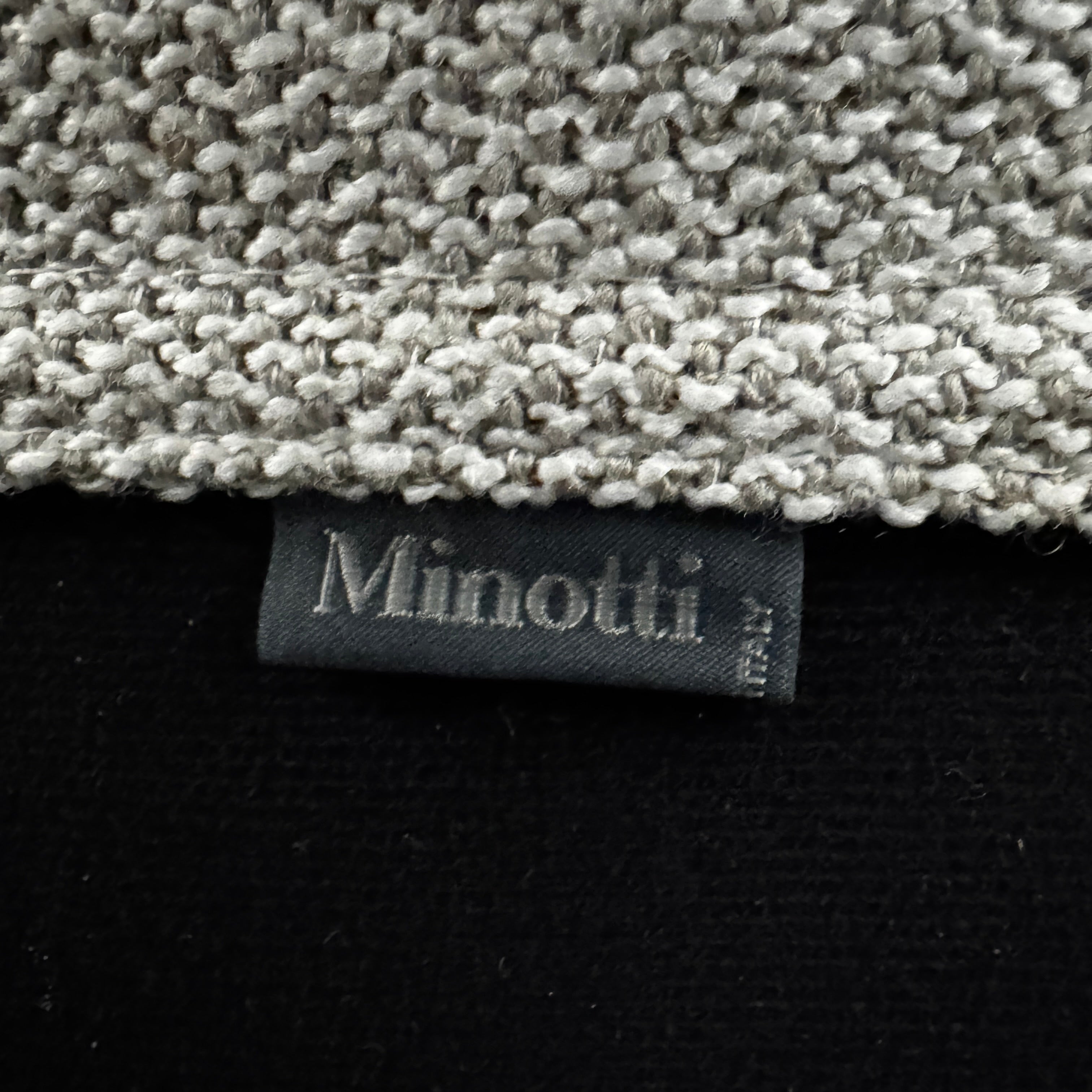 A close-up of knitted fabric featuring a Minotti label on black textile highlights the refined details of modern living furniture like the Minotti Hamilton Love Seat 82".