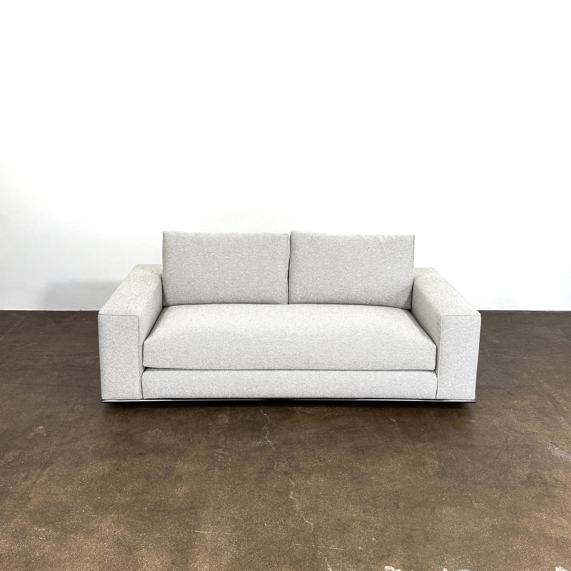 A close-up of knitted fabric featuring a Minotti label on black textile highlights the refined details of modern living furniture like the Minotti Hamilton Love Seat 82".