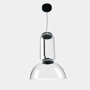 The Flos Noctambule Low Cylinder and Bowl LED Pendant 1 by Flos features a transparent blown crystal glass shade with a cylindrical glass element, suspended from the ceiling by a black cord.
