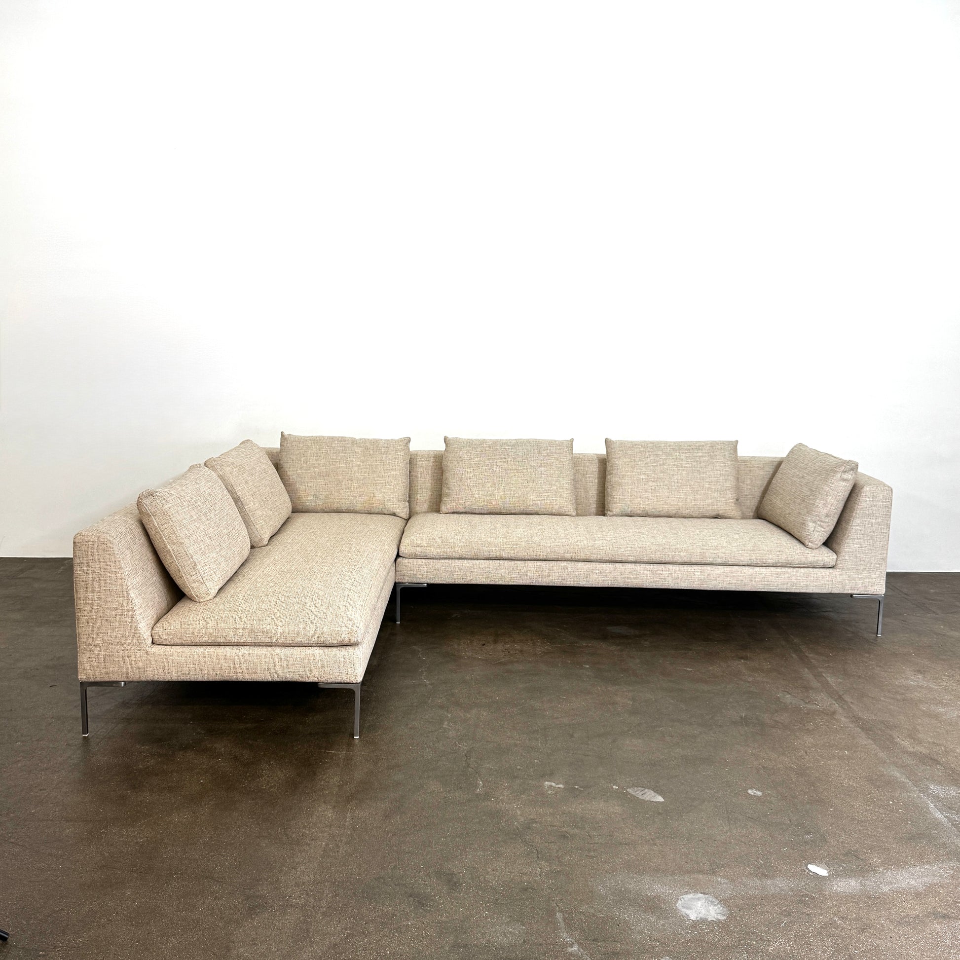 A beige B&B Italia Charles Sectional with five back cushions and metal legs sits on a concrete floor against a plain white wall.