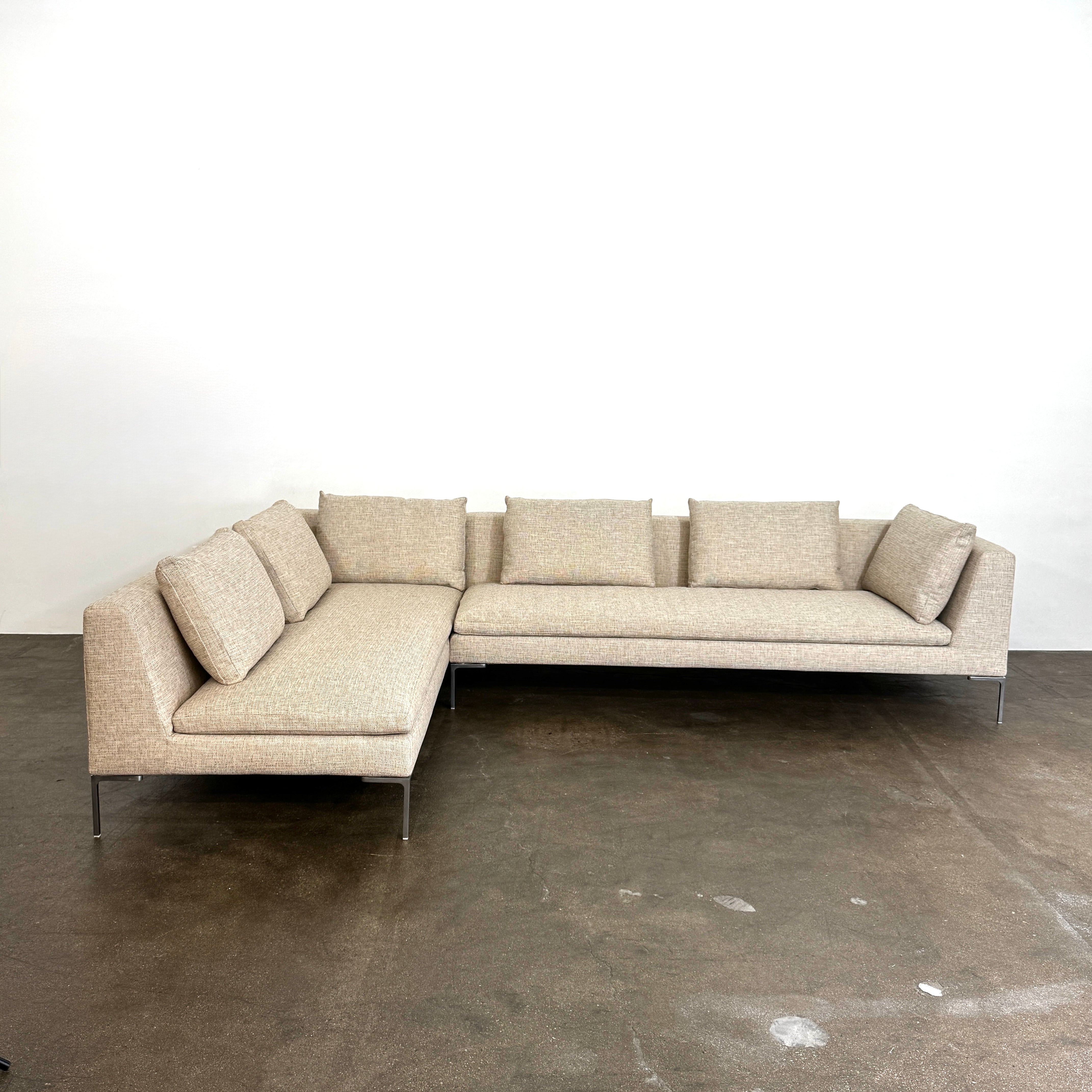 A beige B&B Italia Charles Sectional with five back cushions and metal legs sits on a concrete floor against a plain white wall.