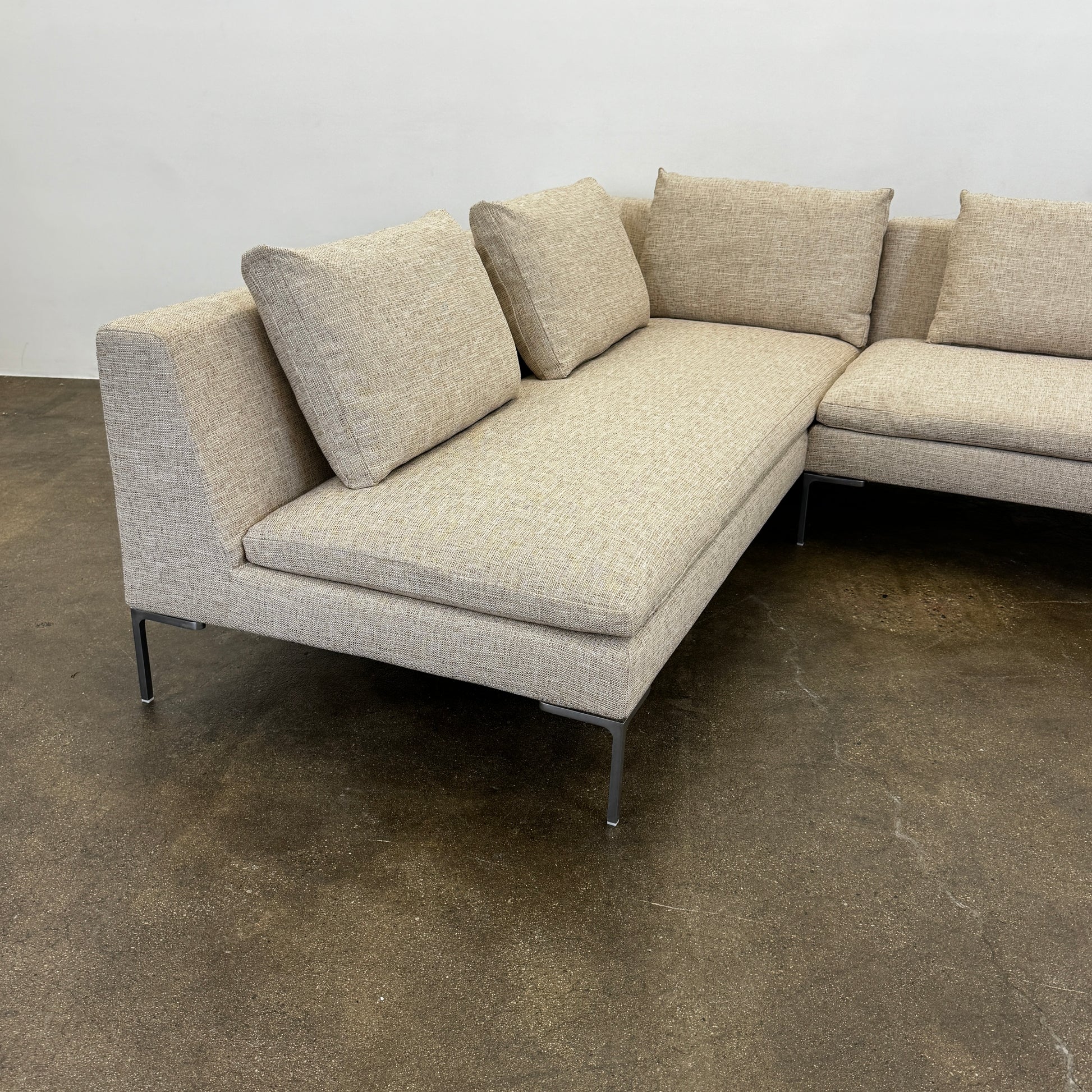 A beige B&B Italia Charles Sectional with five back cushions and metal legs sits on a concrete floor against a plain white wall.