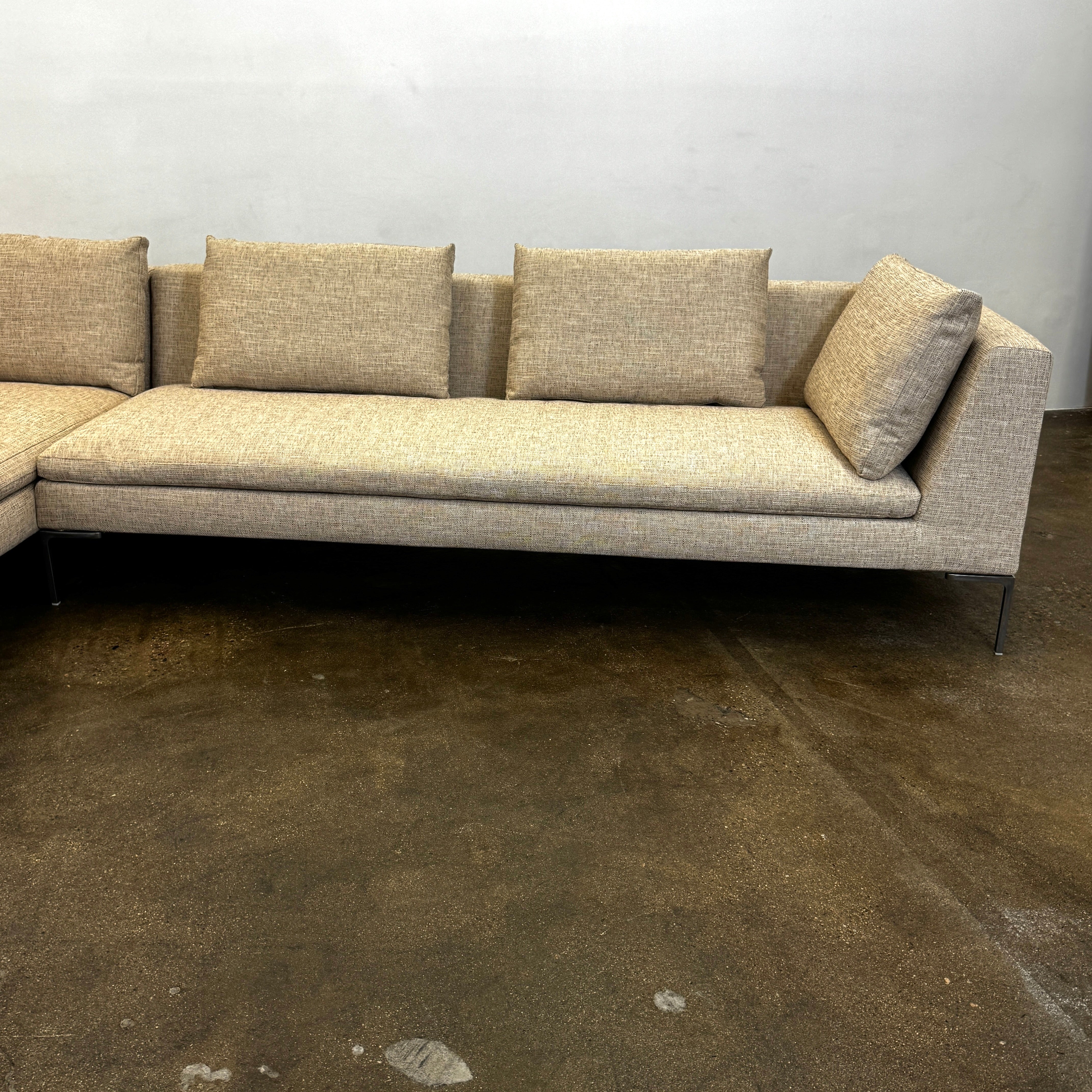 A beige B&B Italia Charles Sectional with five back cushions and metal legs sits on a concrete floor against a plain white wall.