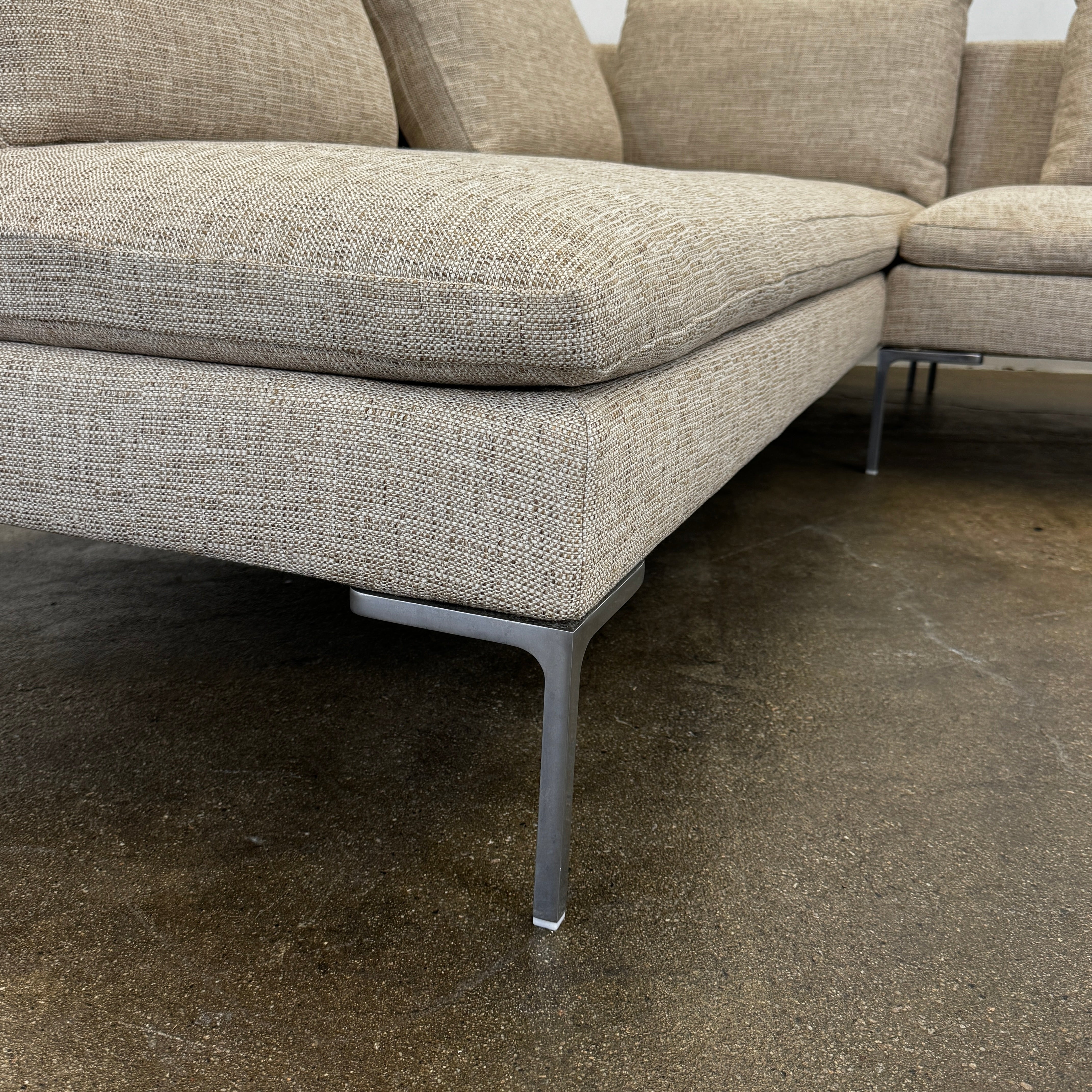 A beige B&B Italia Charles Sectional with five back cushions and metal legs sits on a concrete floor against a plain white wall.