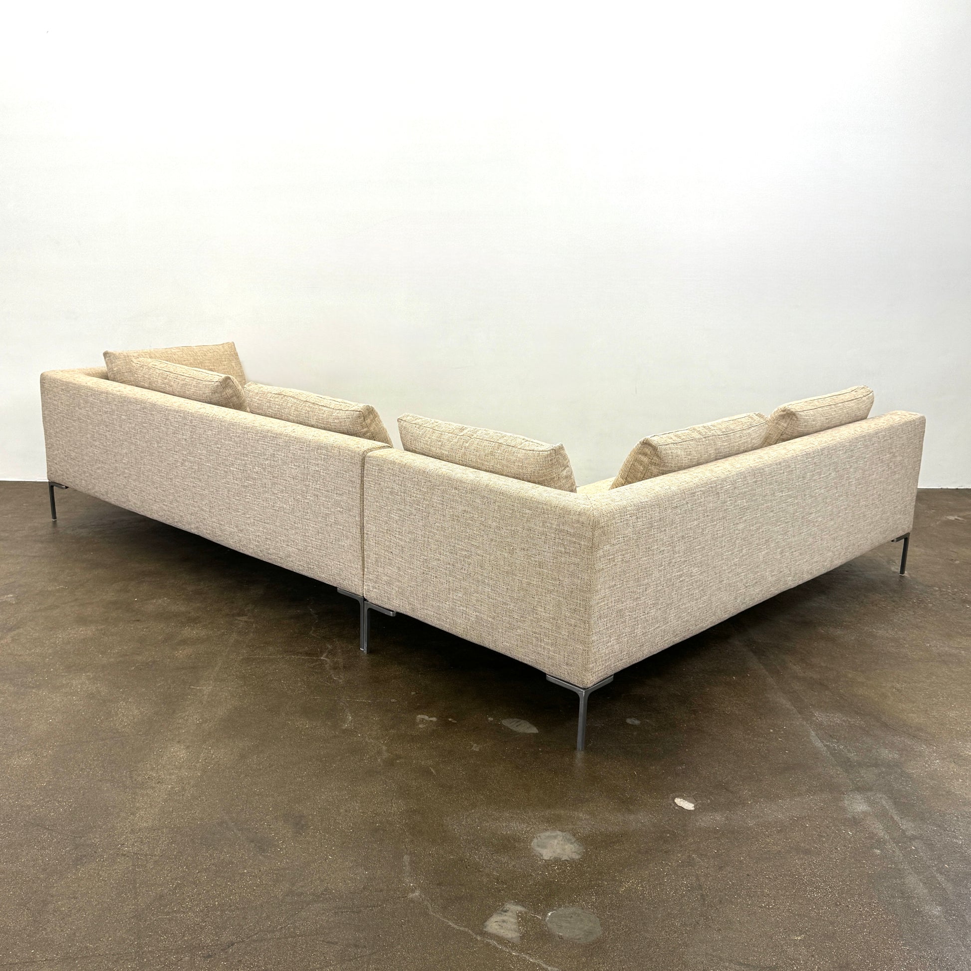 A beige B&B Italia Charles Sectional with five back cushions and metal legs sits on a concrete floor against a plain white wall.
