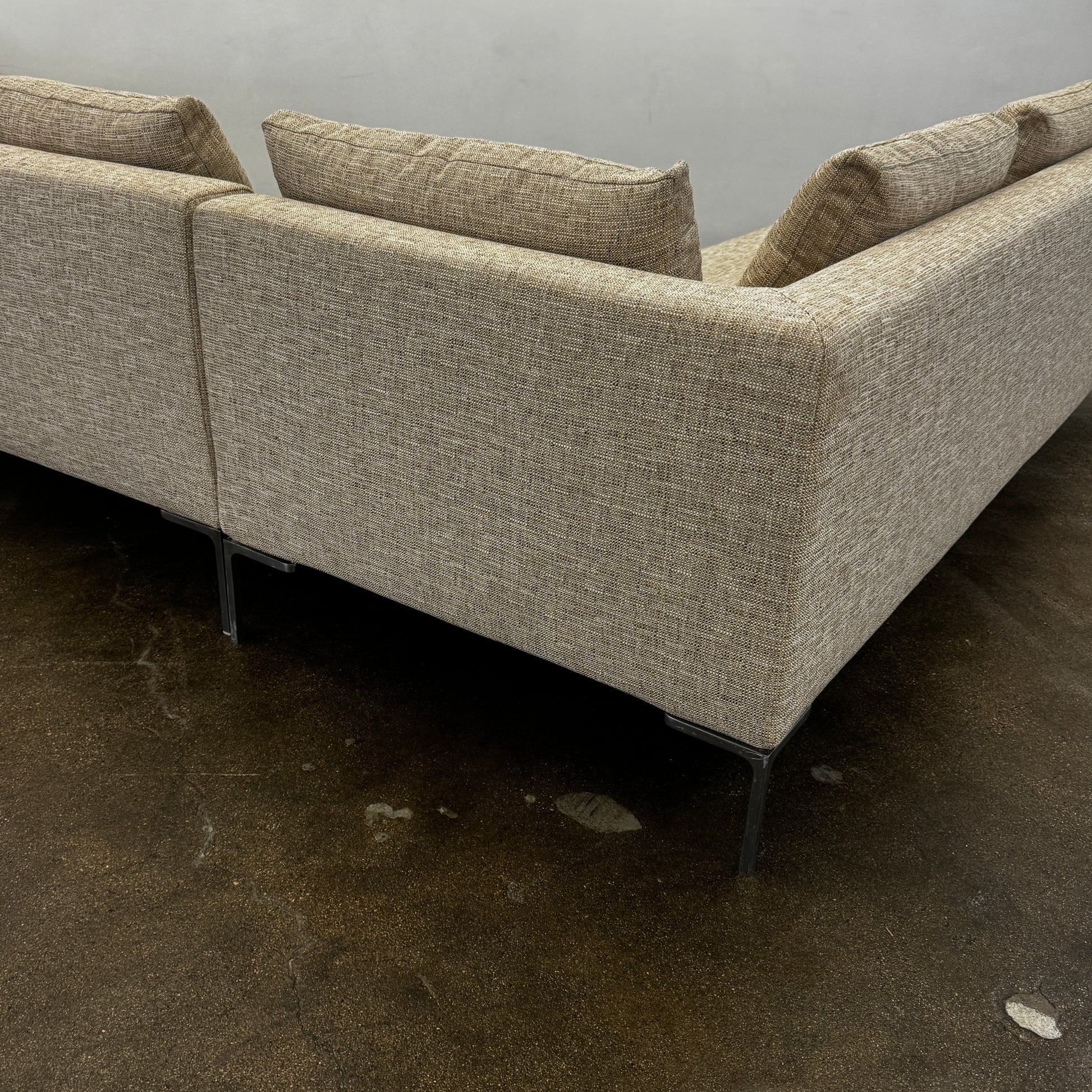 A beige B&B Italia Charles Sectional with five back cushions and metal legs sits on a concrete floor against a plain white wall.