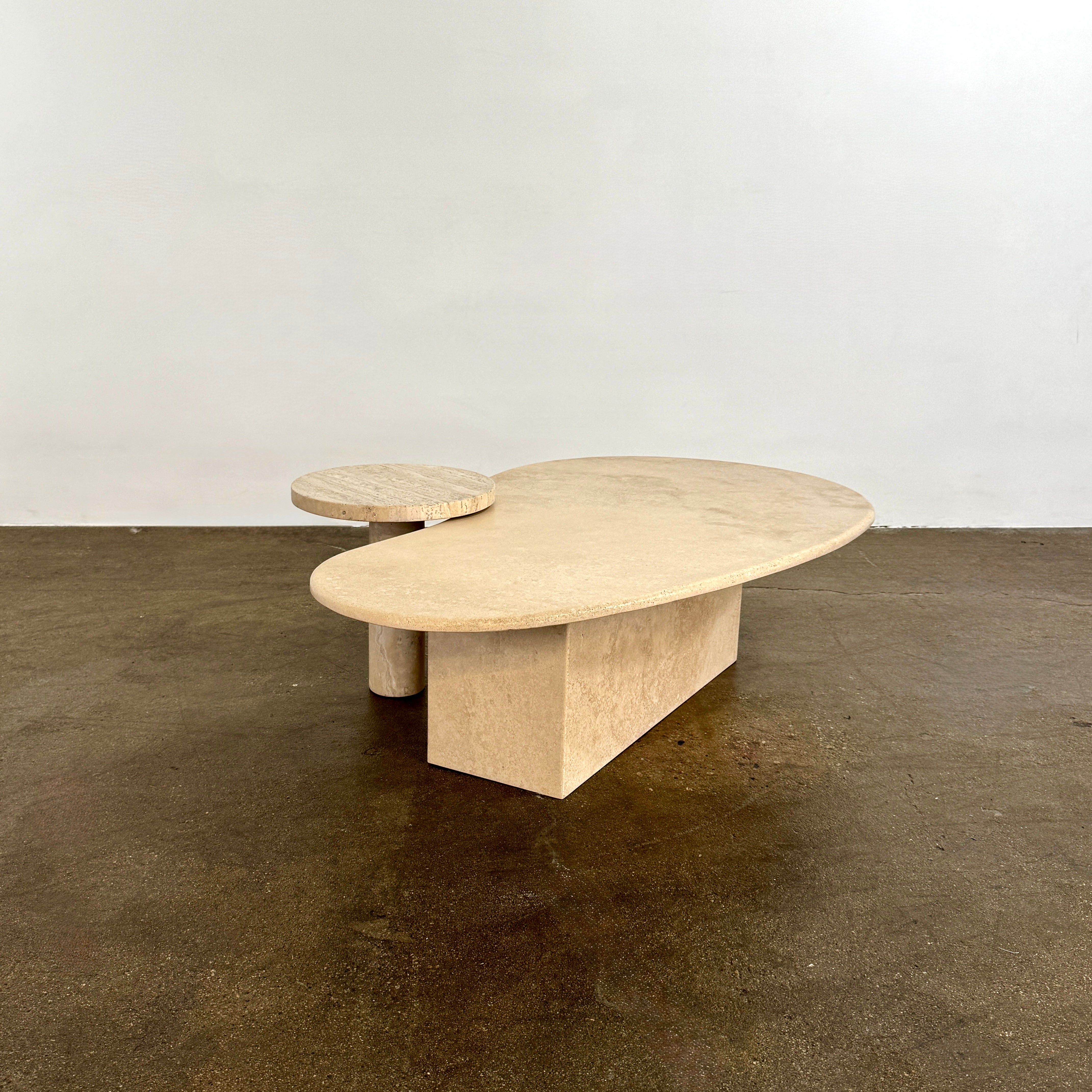 The Custom Travertine Coffee Table Set by Custom features two beige stone surfaces—one oval, one round—supported by solid travertine legs, offering sculptural elegance and modern style to any space.