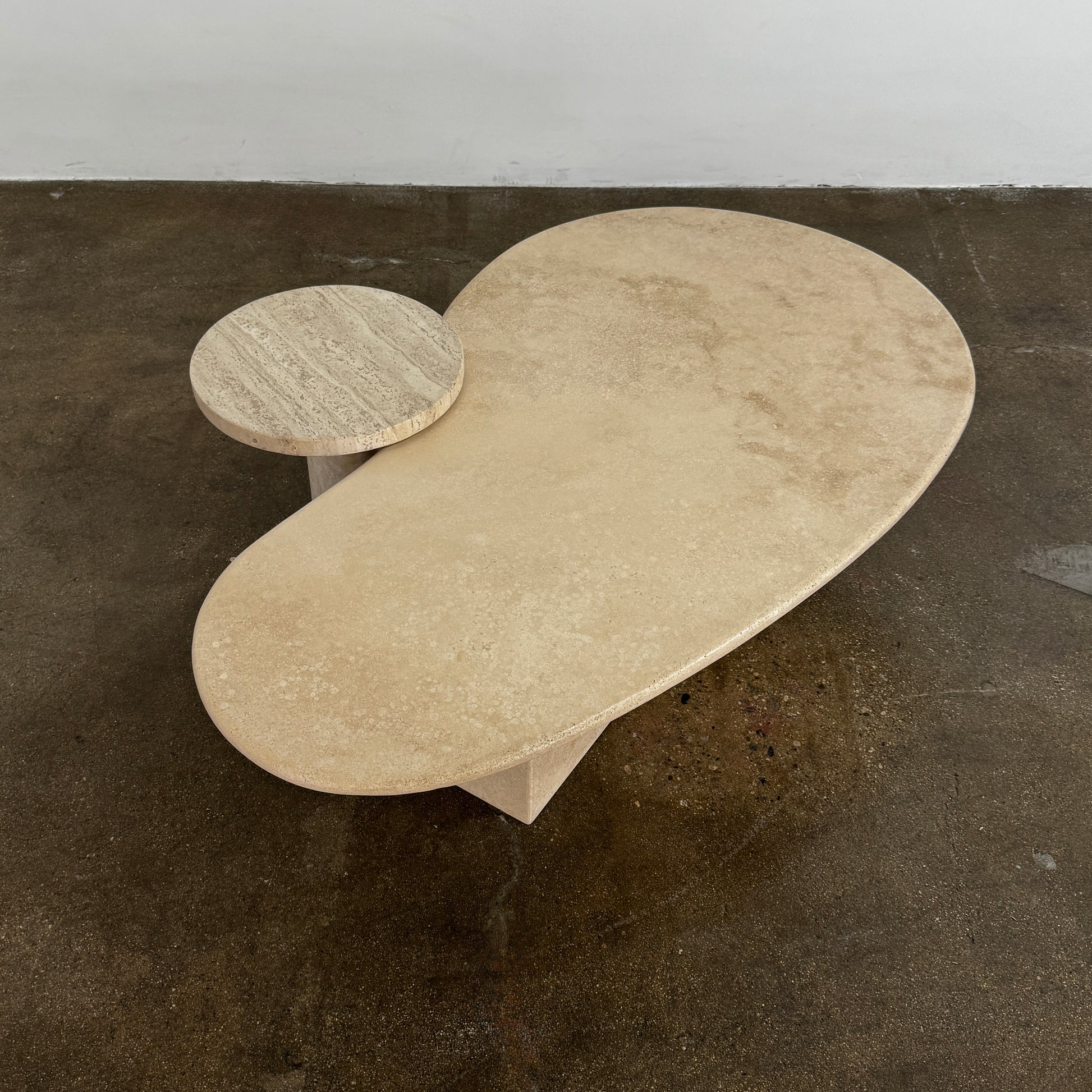 The Custom Travertine Coffee Table Set by Custom features two beige stone surfaces—one oval, one round—supported by solid travertine legs, offering sculptural elegance and modern style to any space.