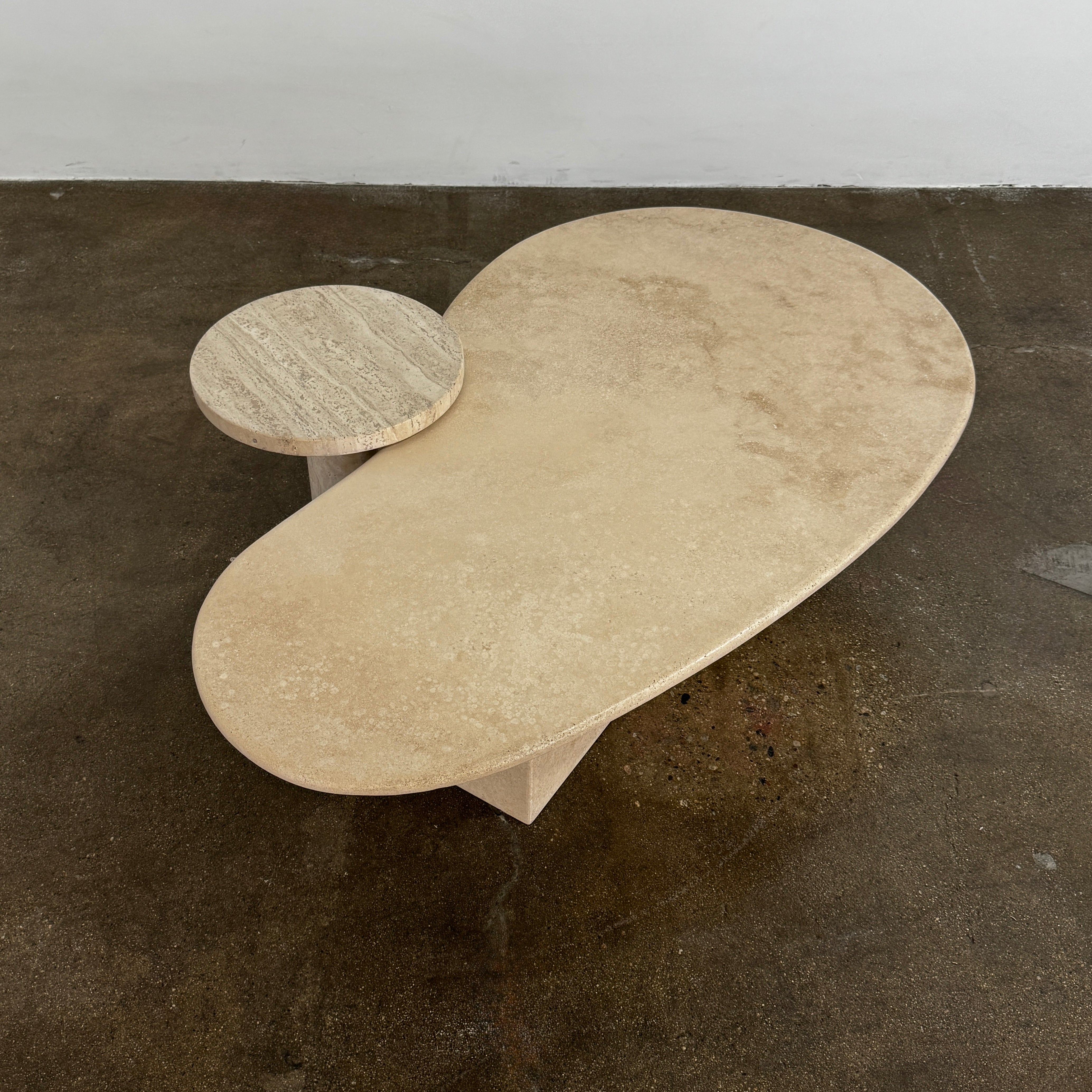 The Custom Travertine Coffee Table Set by Custom features two beige stone surfaces—one oval, one round—supported by solid travertine legs, offering sculptural elegance and modern style to any space.