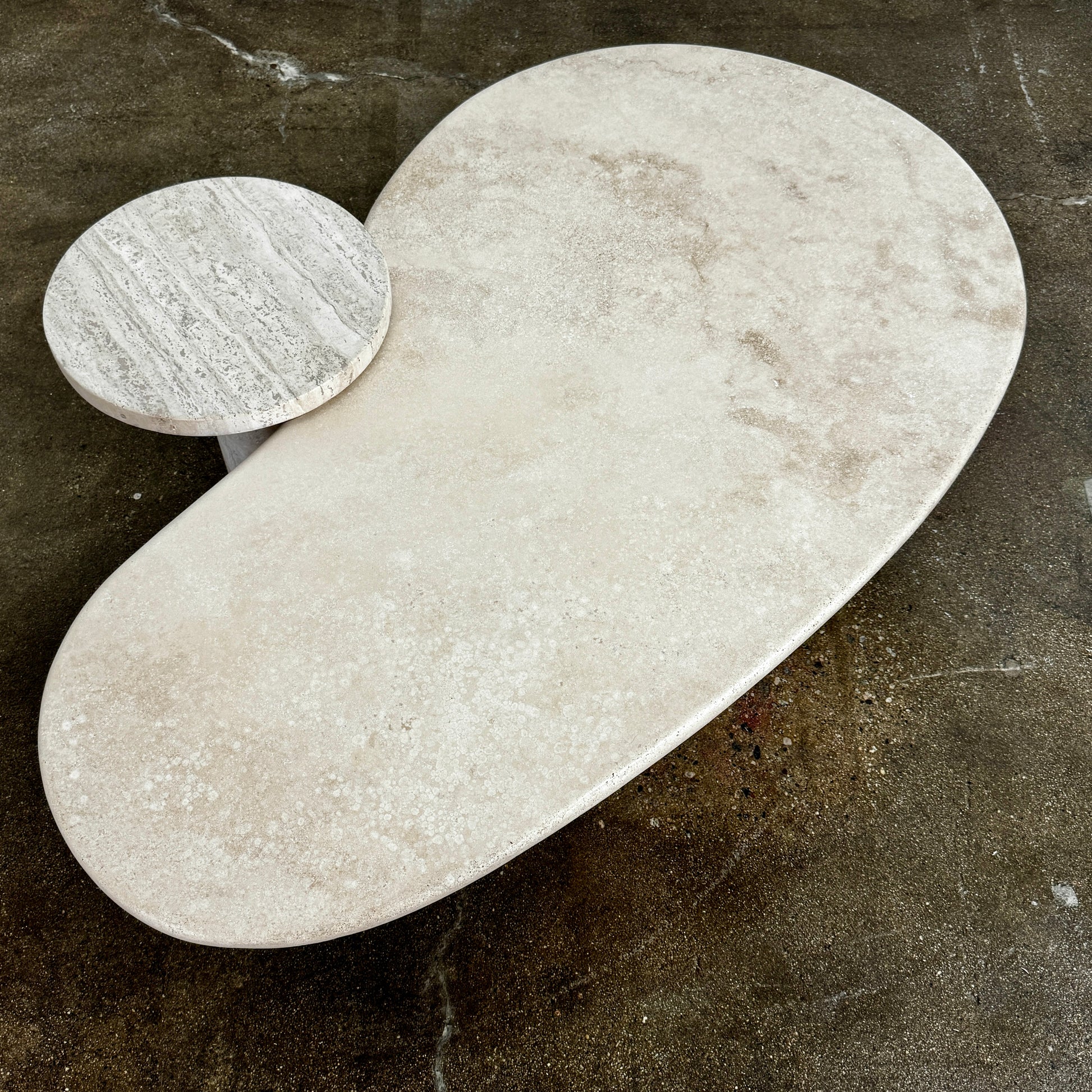 The Custom Travertine Coffee Table Set by Custom features two beige stone surfaces—one oval, one round—supported by solid travertine legs, offering sculptural elegance and modern style to any space.