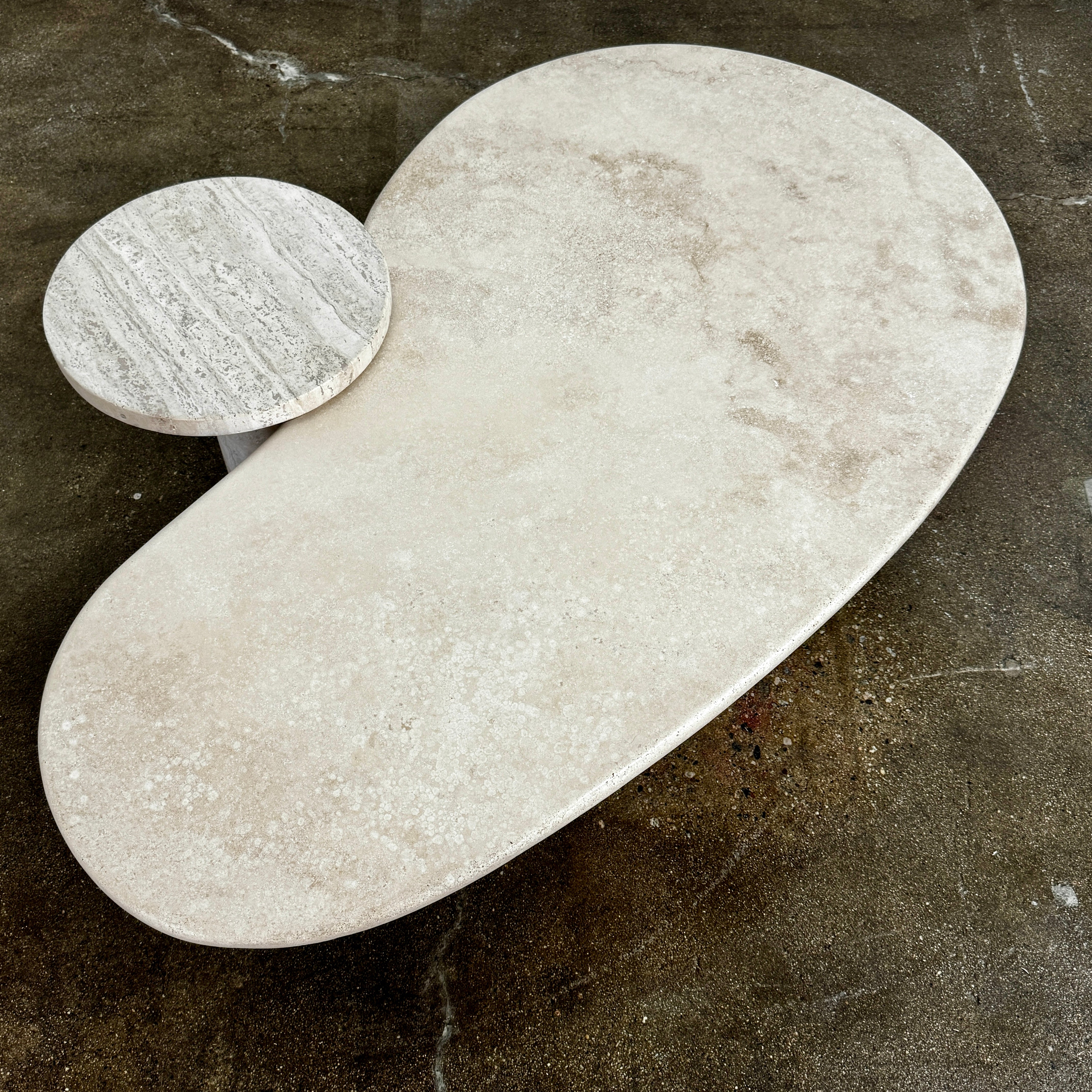 The Custom Travertine Coffee Table Set by Custom features two beige stone surfaces—one oval, one round—supported by solid travertine legs, offering sculptural elegance and modern style to any space.