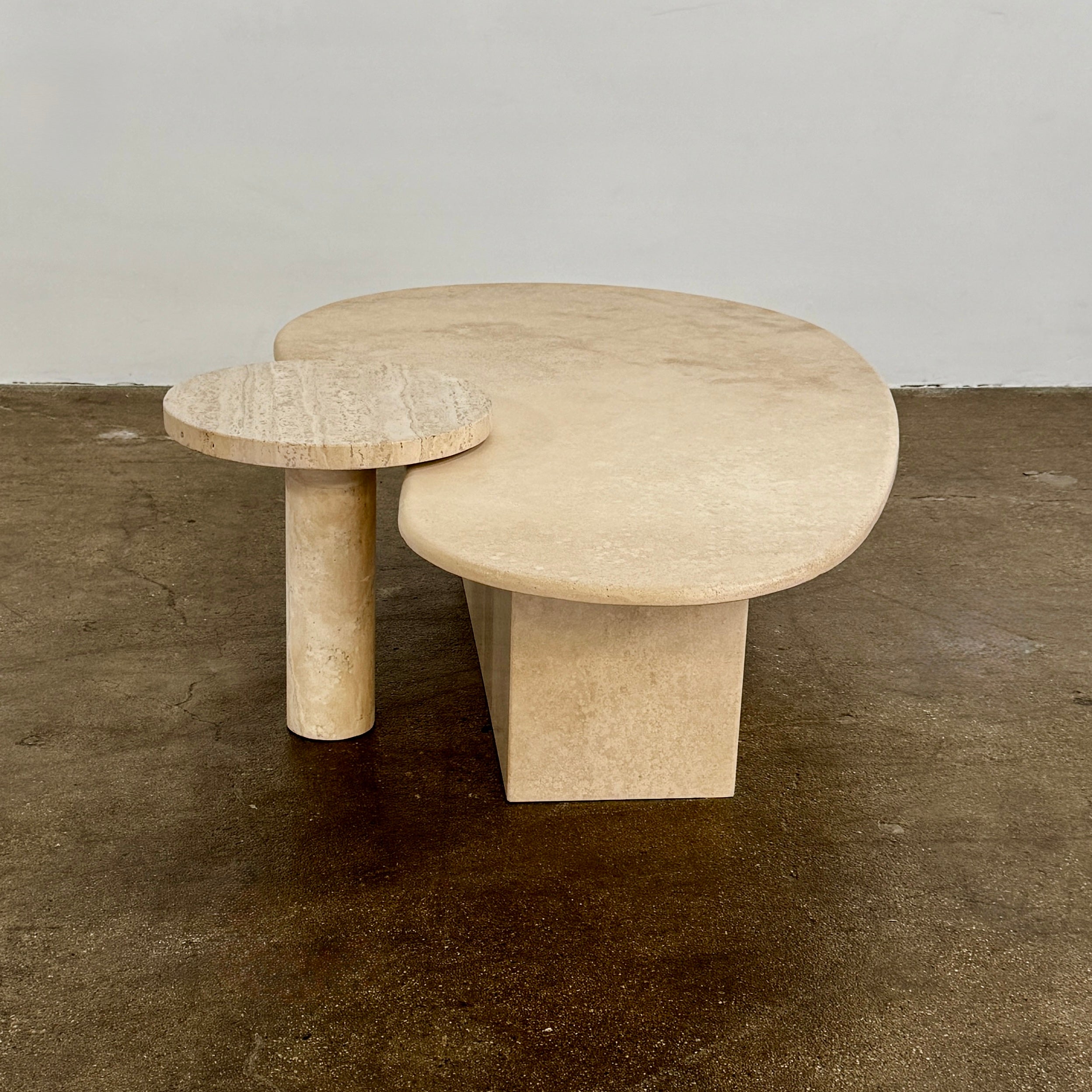 The Custom Travertine Coffee Table Set by Custom features two beige stone surfaces—one oval, one round—supported by solid travertine legs, offering sculptural elegance and modern style to any space.