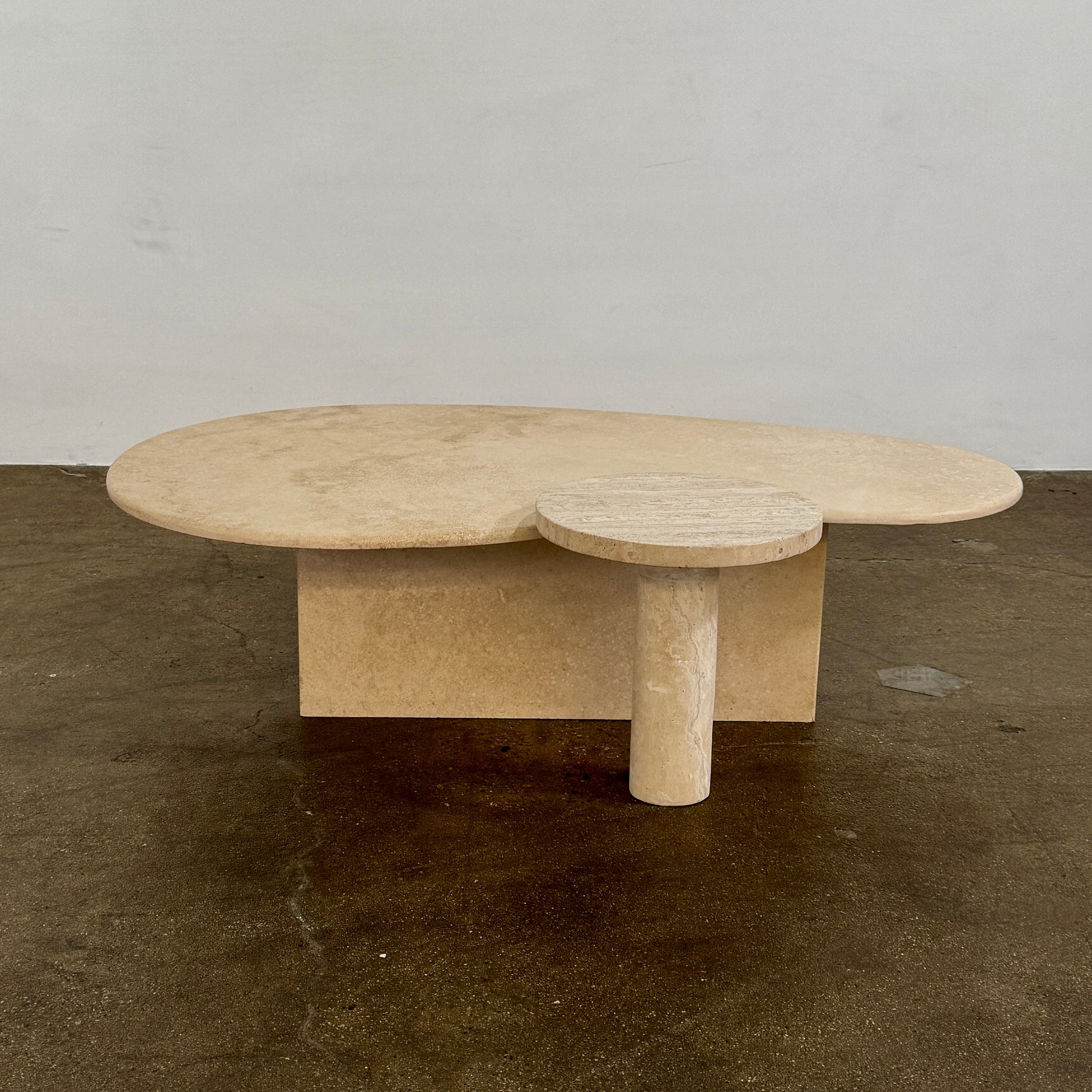 The Custom Travertine Coffee Table Set by Custom features two beige stone surfaces—one oval, one round—supported by solid travertine legs, offering sculptural elegance and modern style to any space.