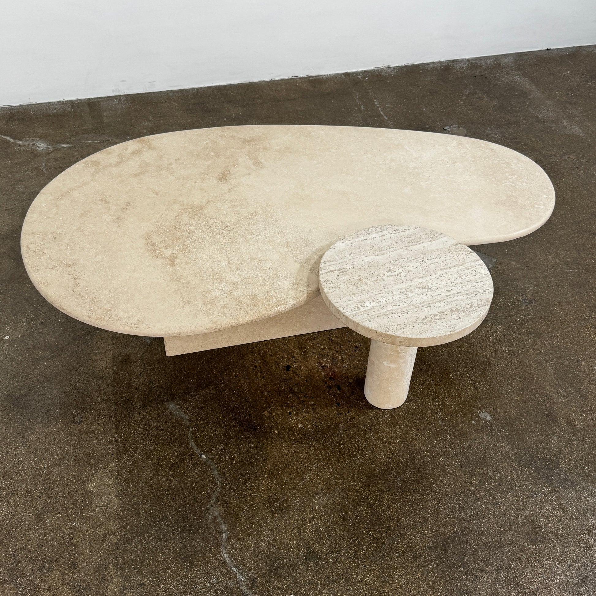 The Custom Travertine Coffee Table Set by Custom features two beige stone surfaces—one oval, one round—supported by solid travertine legs, offering sculptural elegance and modern style to any space.