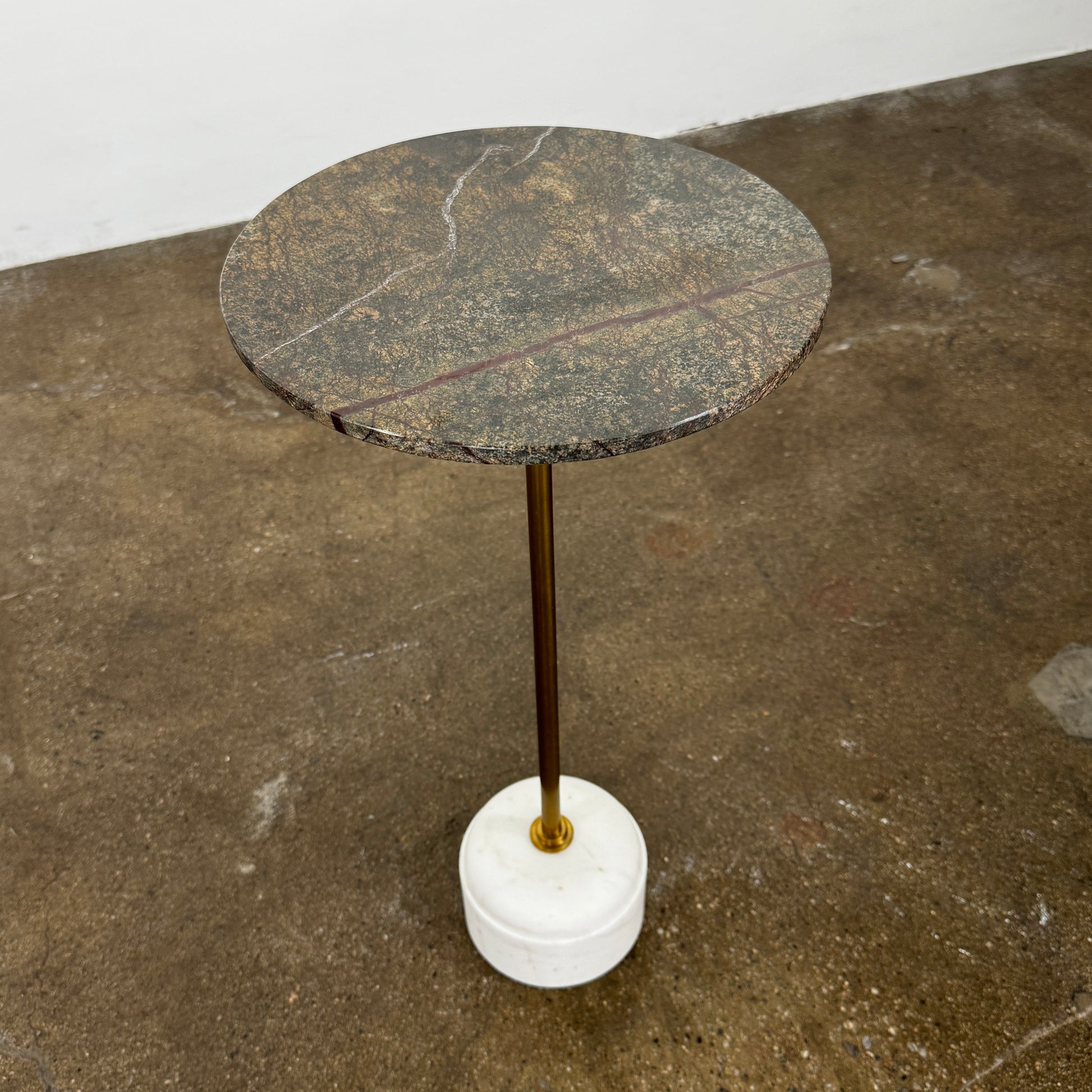 The Soho Home Fleet Side Table by Soho Home features a dark Verde Bosque marble top, slender antique brass stem, and a white cylindrical marble base, shown against a plain light background.