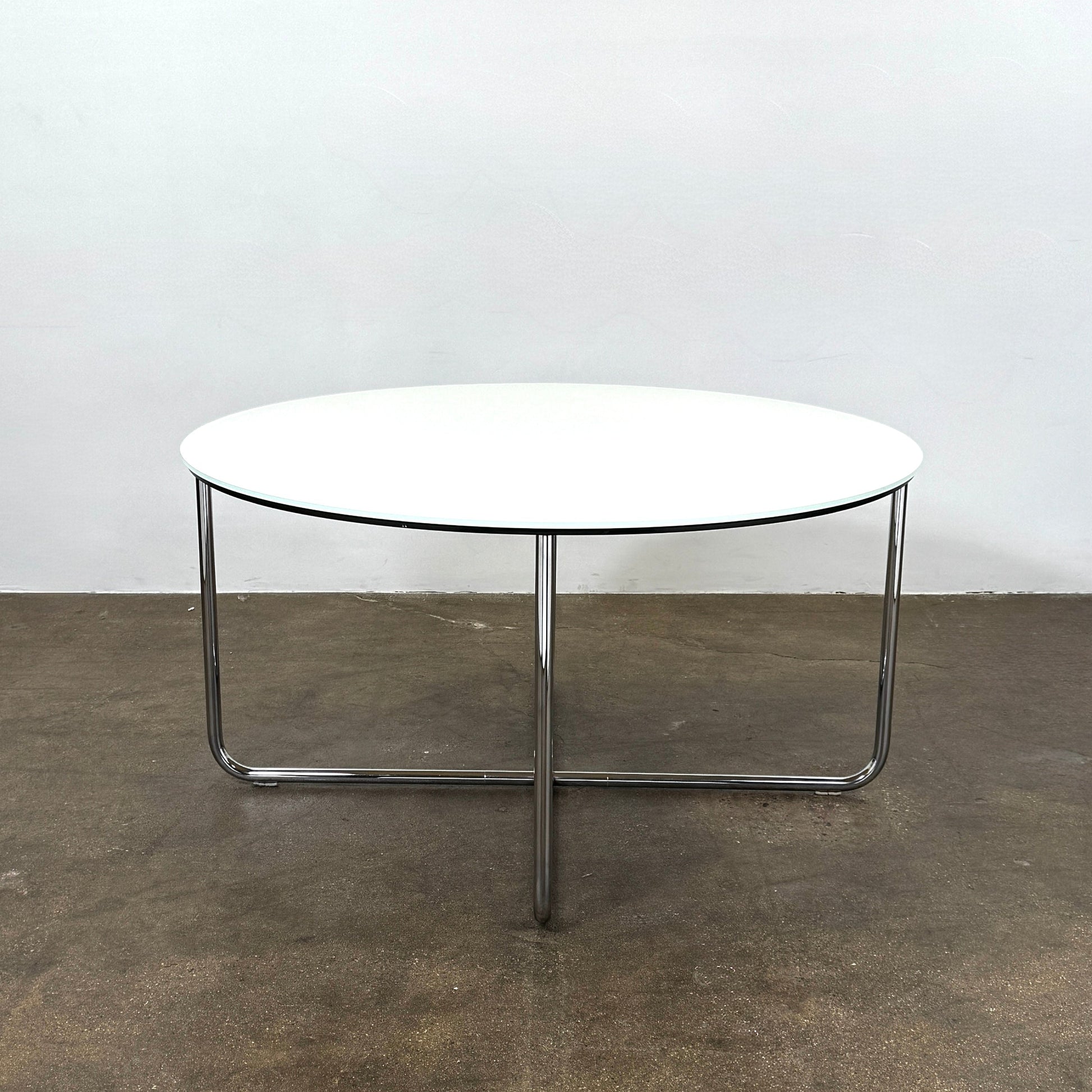 The Minotti Louis Round Dining Table features a white top and a modern metal base with three intersecting legs, reflecting Minotti’s signature style.