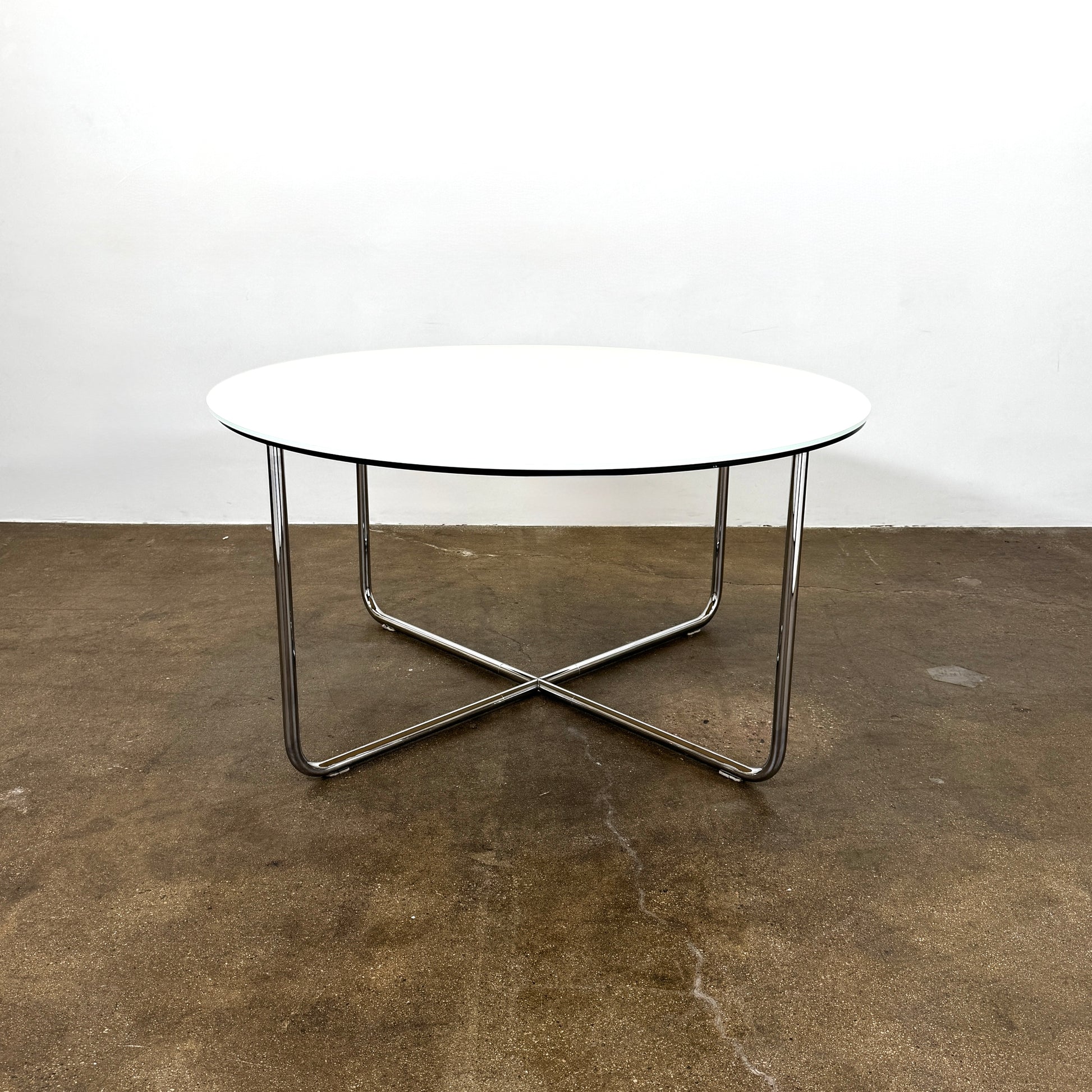 The Minotti Louis Round Dining Table features a white top and a modern metal base with three intersecting legs, reflecting Minotti’s signature style.