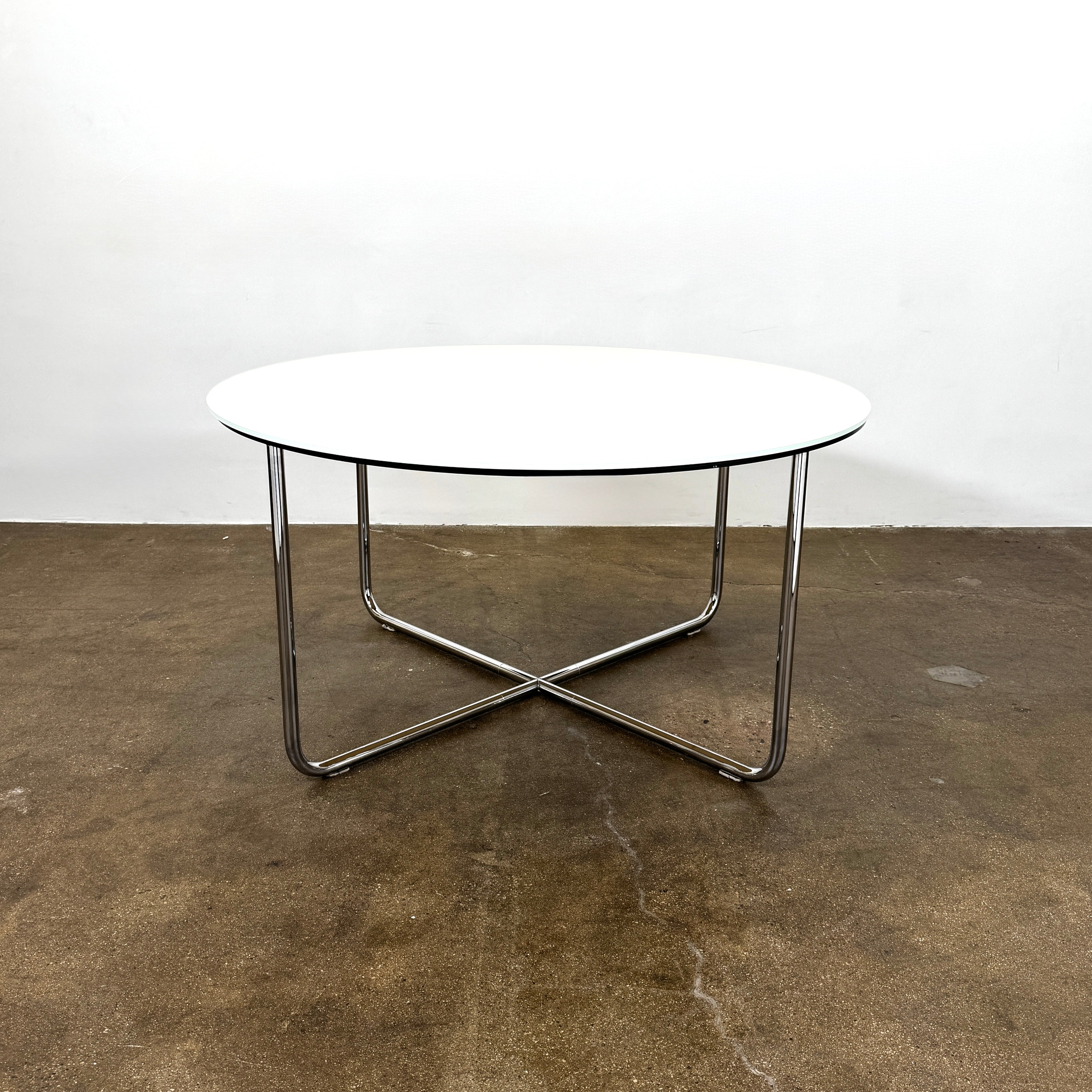 The Minotti Louis Round Dining Table features a white top and a modern metal base with three intersecting legs, reflecting Minotti’s signature style.