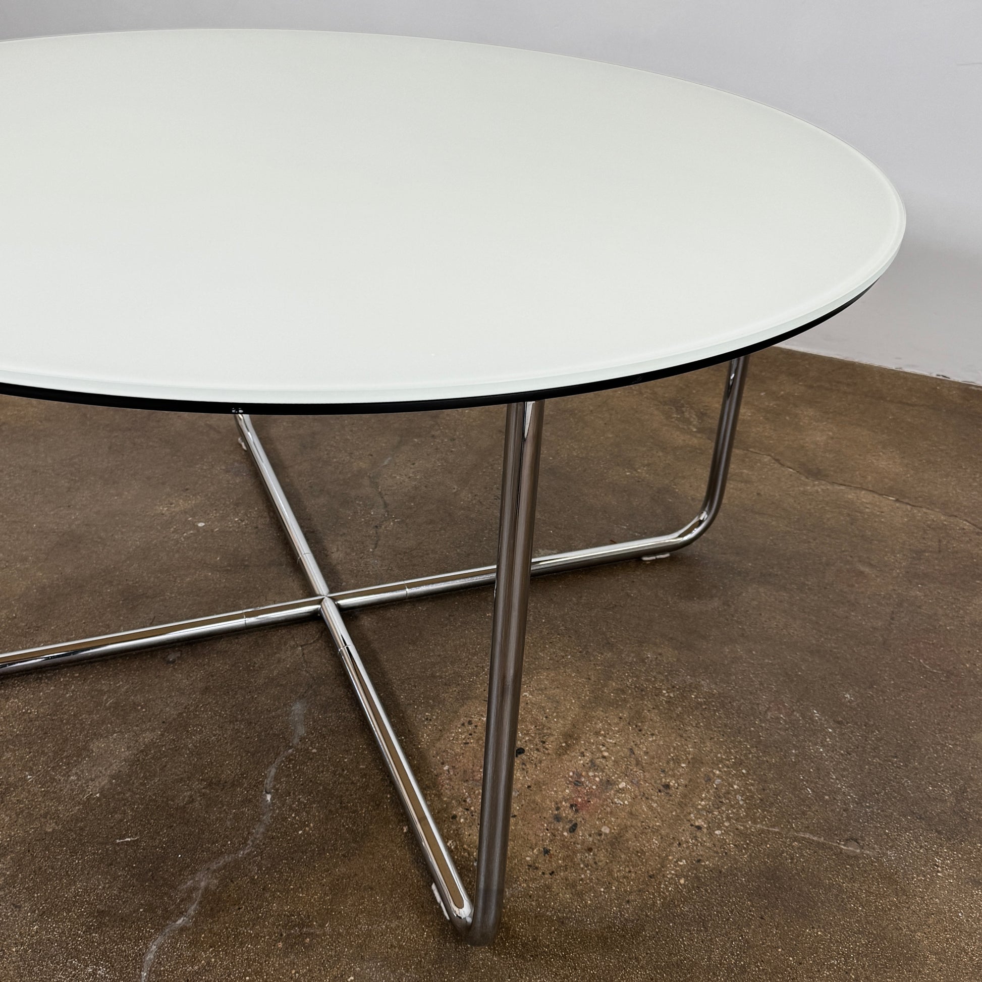 The Minotti Louis Round Dining Table features a white top and a modern metal base with three intersecting legs, reflecting Minotti’s signature style.