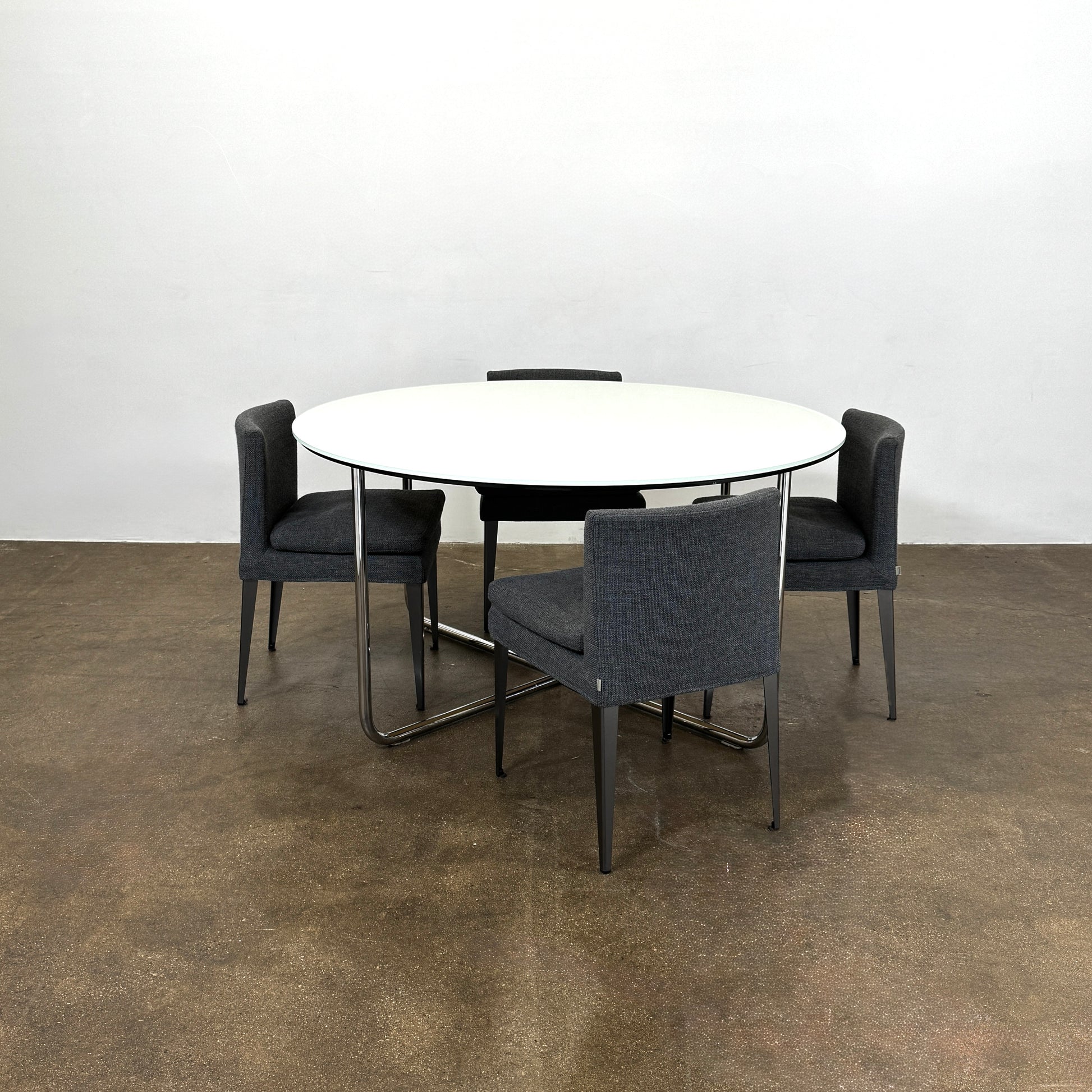 The Minotti Louis Round Dining Table features a white top and a modern metal base with three intersecting legs, reflecting Minotti’s signature style.