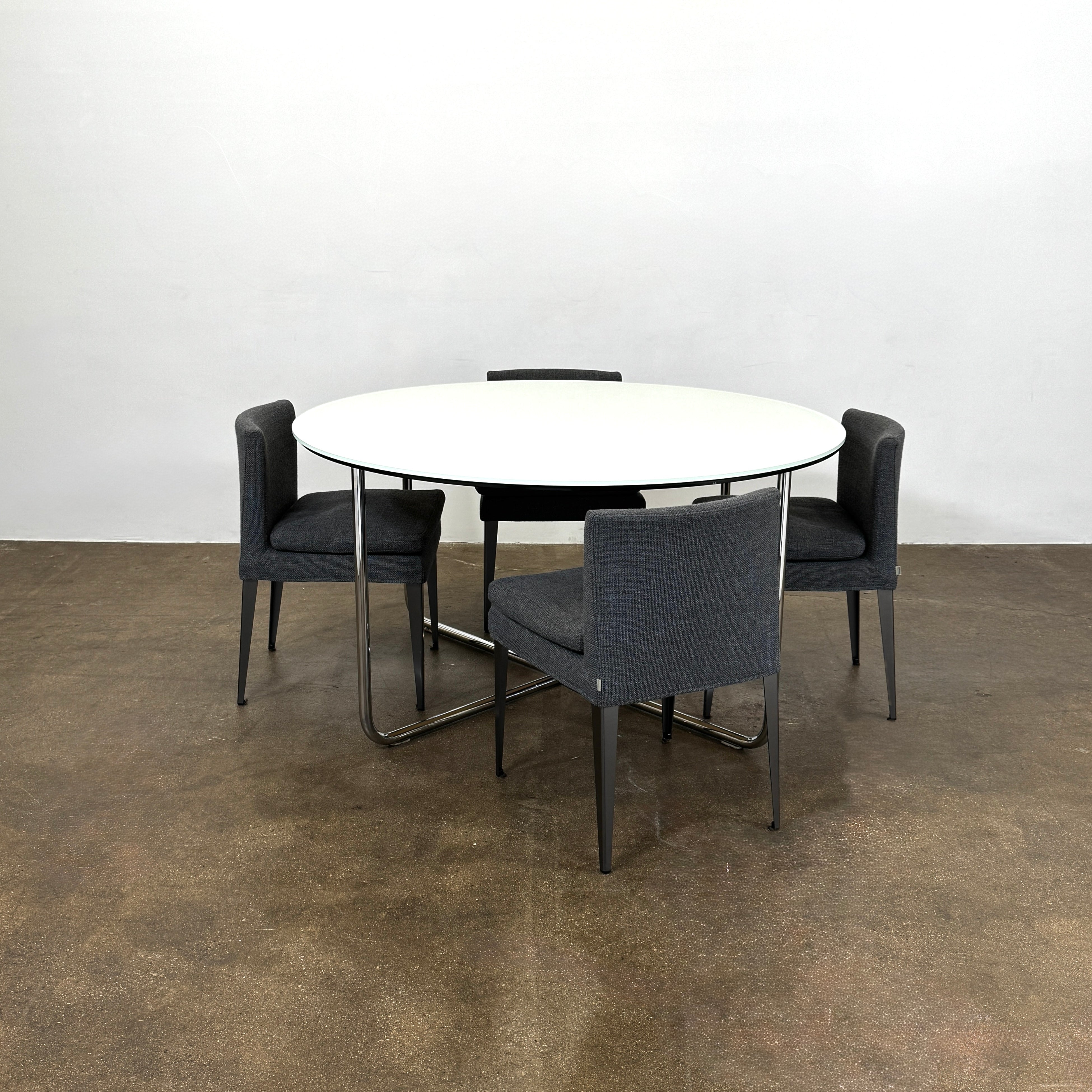 The Minotti Louis Round Dining Table features a white top and a modern metal base with three intersecting legs, reflecting Minotti’s signature style.