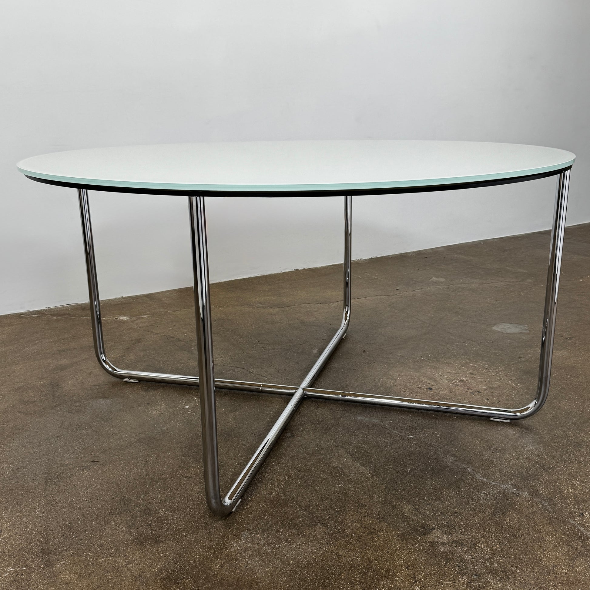 The Minotti Louis Round Dining Table features a white top and a modern metal base with three intersecting legs, reflecting Minotti’s signature style.