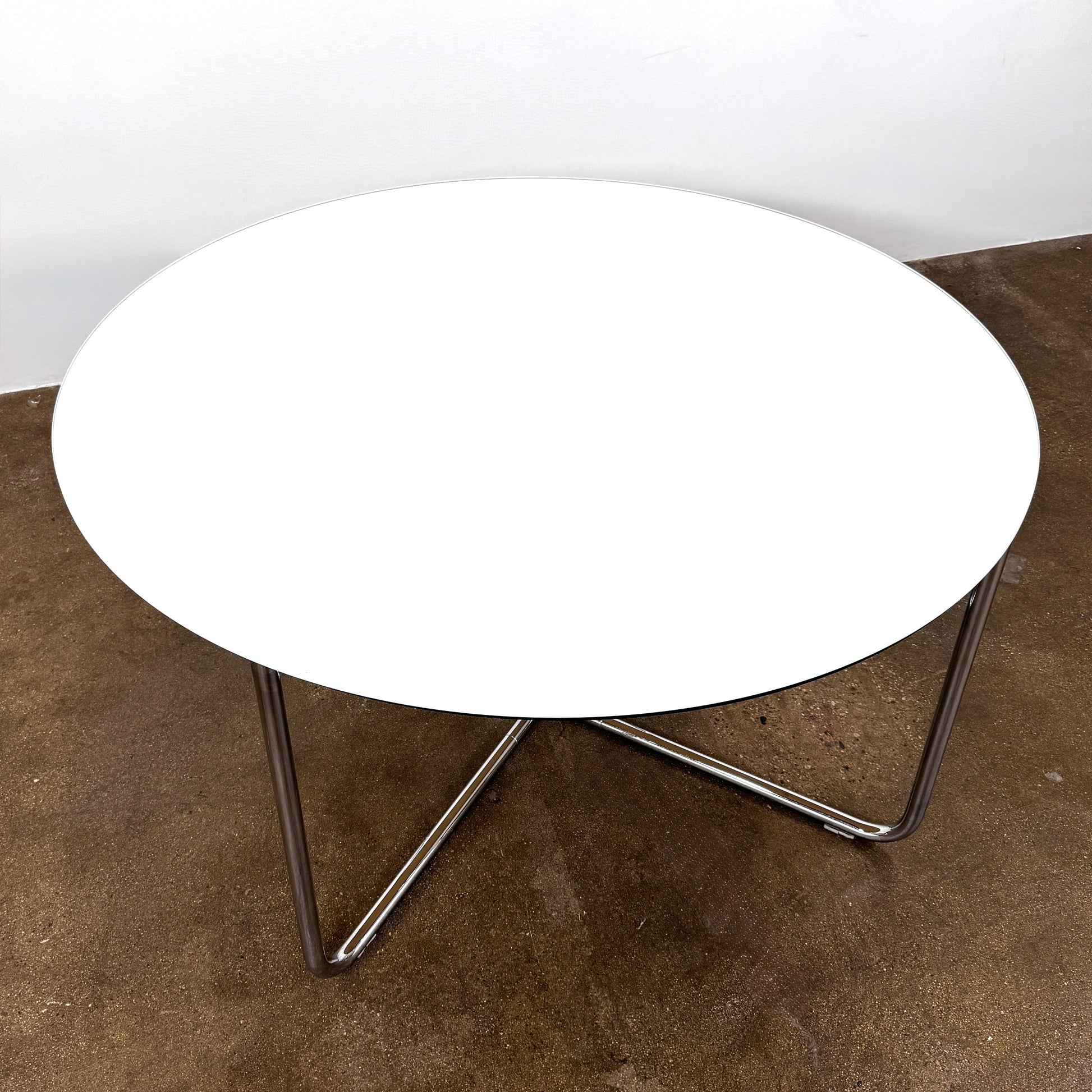 The Minotti Louis Round Dining Table features a white top and a modern metal base with three intersecting legs, reflecting Minotti’s signature style.