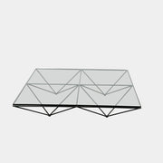 A B&B Italia Alanda Coffee Table with a glass top and metal frame sits on a polished concrete floor, with a magazine placed on its corner.