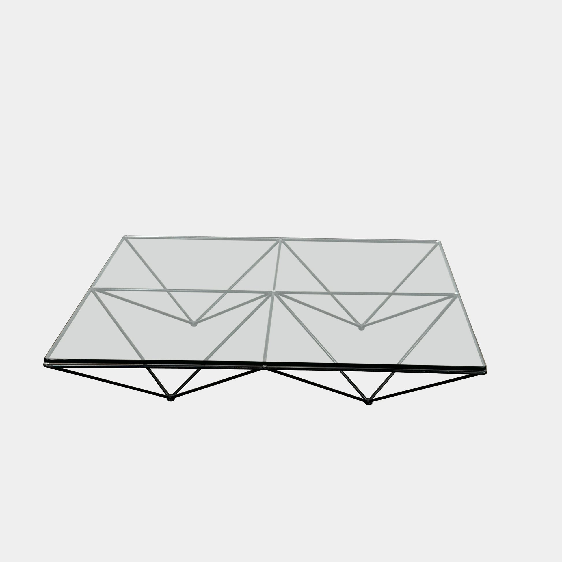 A B&B Italia Alanda Coffee Table with a glass top and metal frame sits on a polished concrete floor, with a magazine placed on its corner.