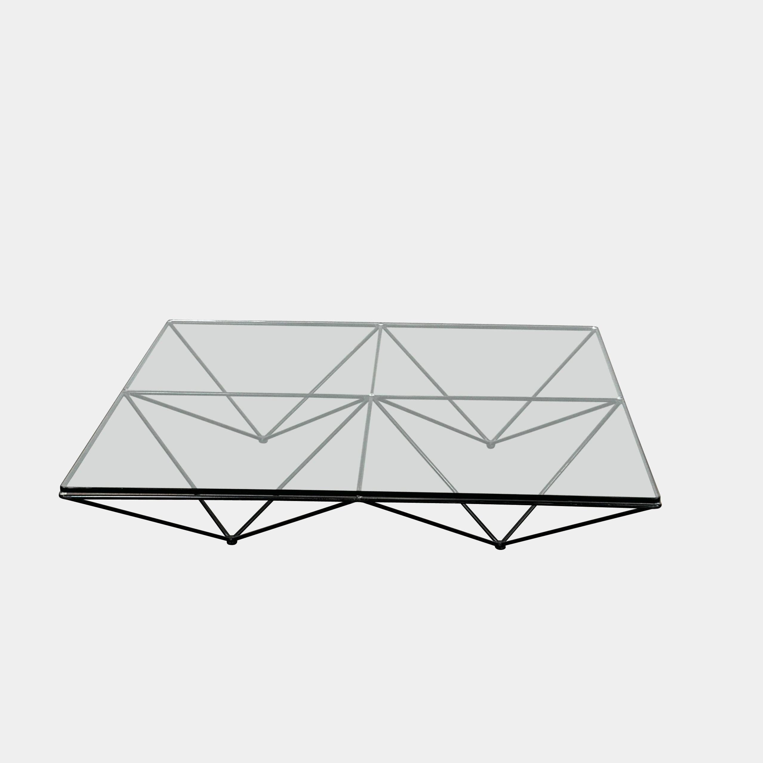 A B&B Italia Alanda Coffee Table with a glass top and metal frame sits on a polished concrete floor, with a magazine placed on its corner.