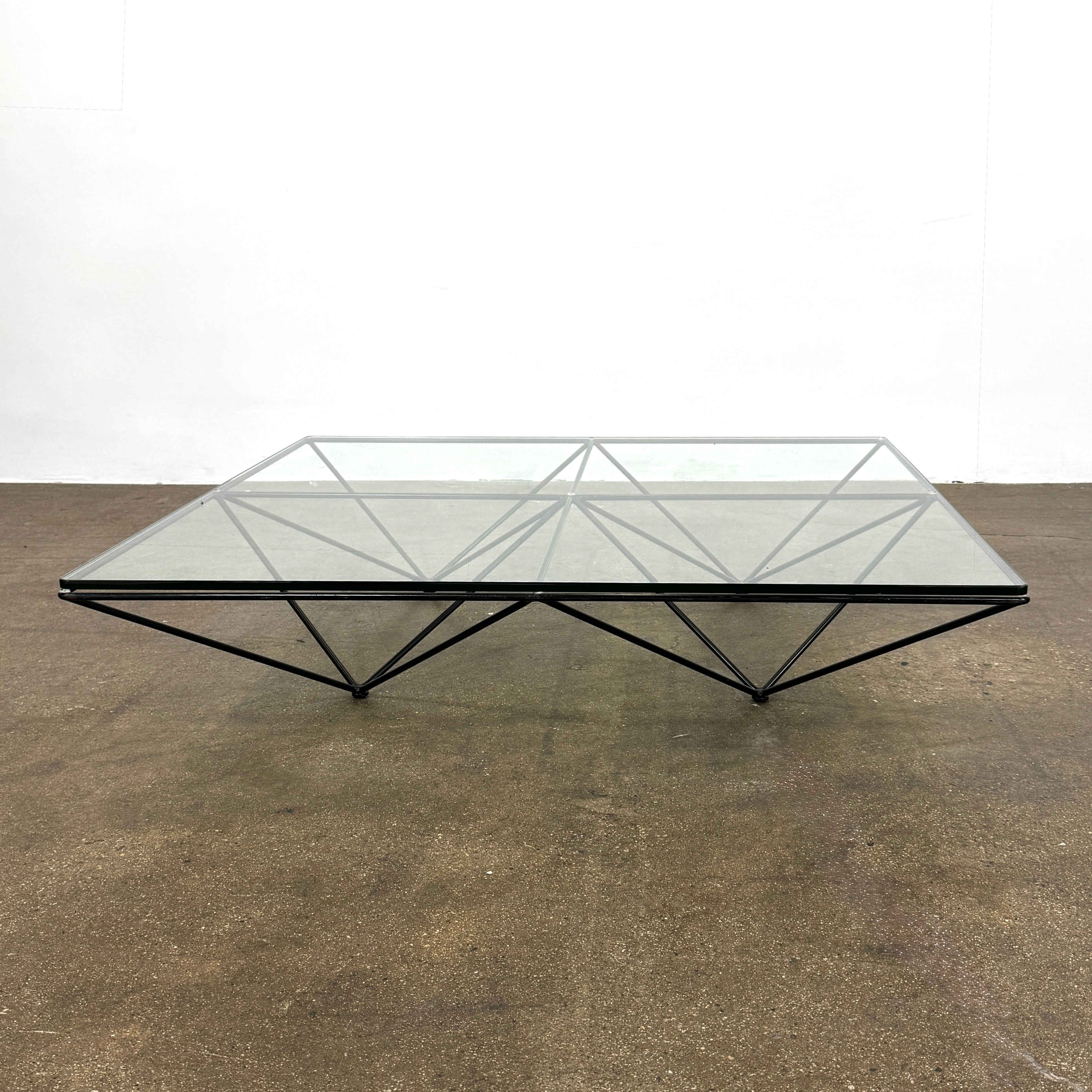 A B&B Italia Alanda Coffee Table with a glass top and metal frame sits on a polished concrete floor, with a magazine placed on its corner.