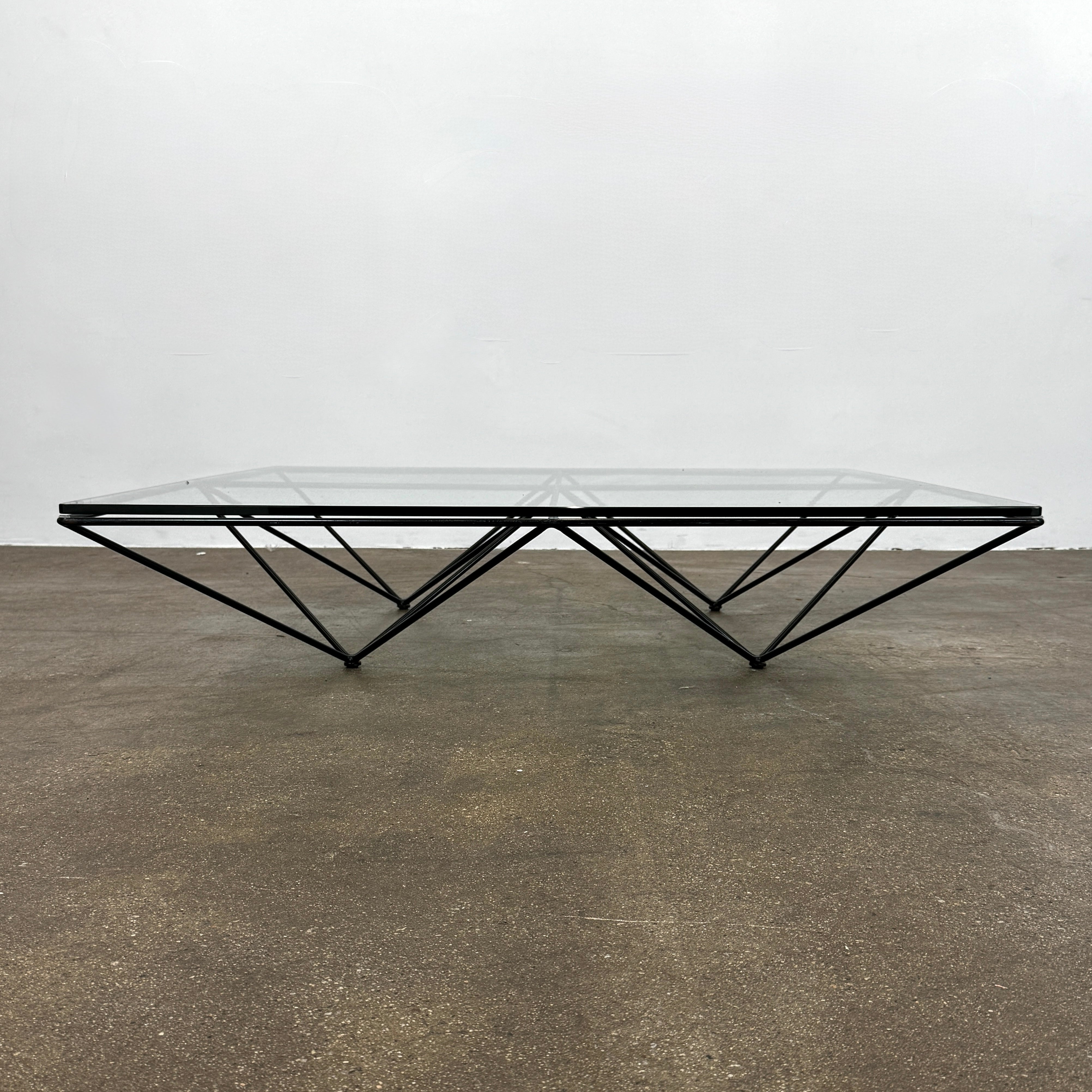 A B&B Italia Alanda Coffee Table with a glass top and metal frame sits on a polished concrete floor, with a magazine placed on its corner.