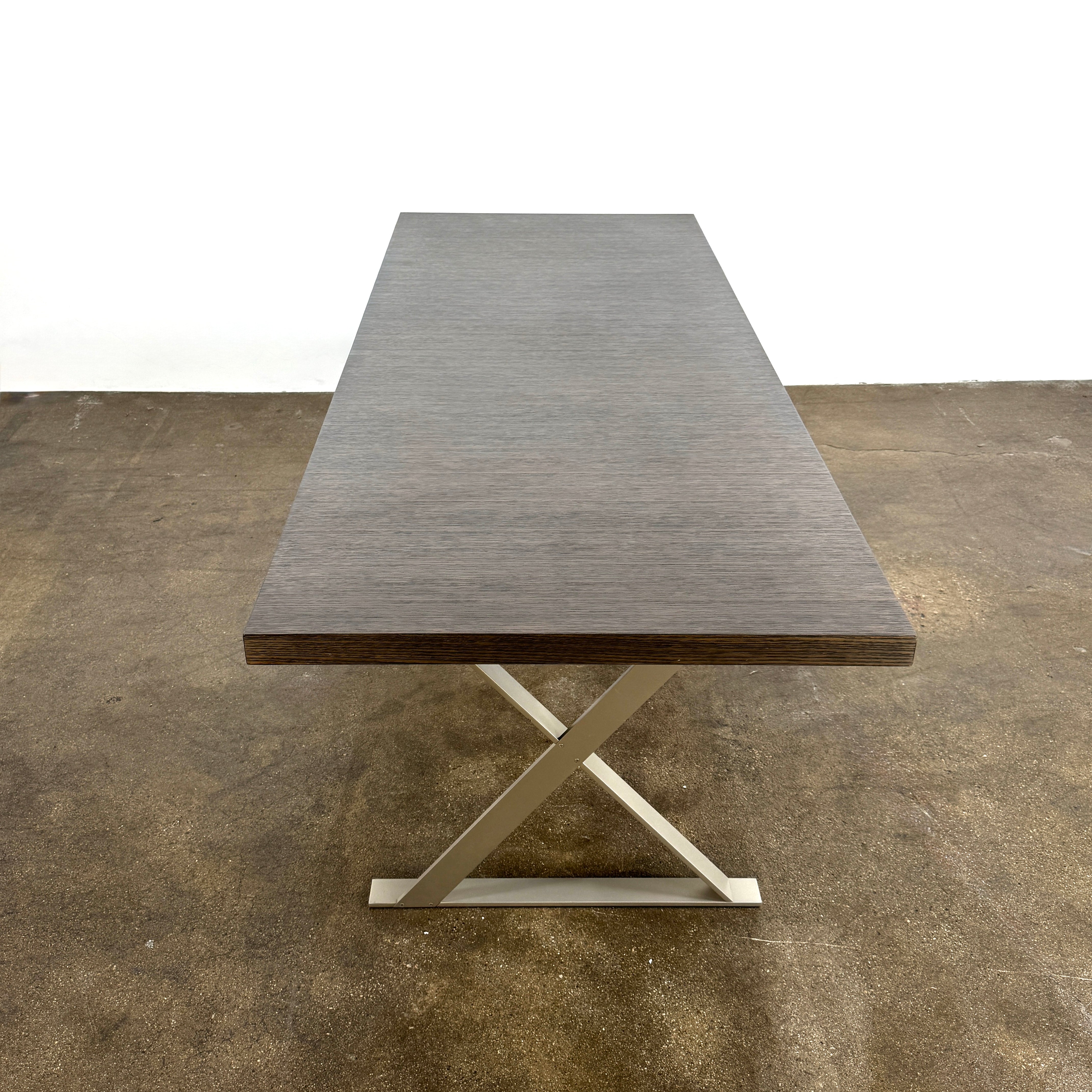 The Maxalto Max Table Grey Oak by Maxalto features a grey oak wooden top, metal legs, and an angular modern design—ideal for enhancing any dining space. Displayed on a plain white background.