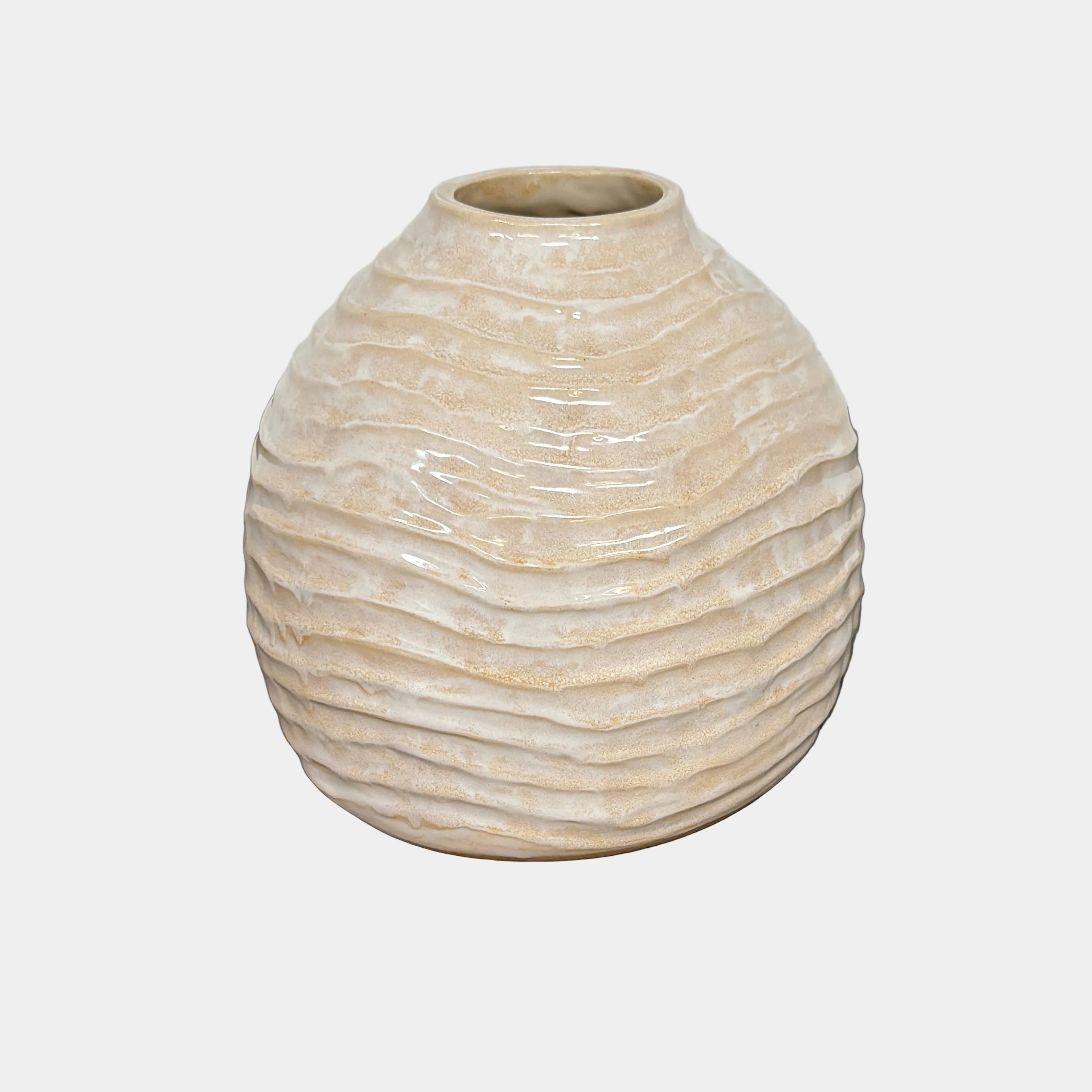 The Sofi Ceramics Tropez Vase by Artist, featuring a round beige shape with textured horizontal ridges, sits on a dark wooden surface against a light gray background, highlighting the elegance of sculptured vessels.