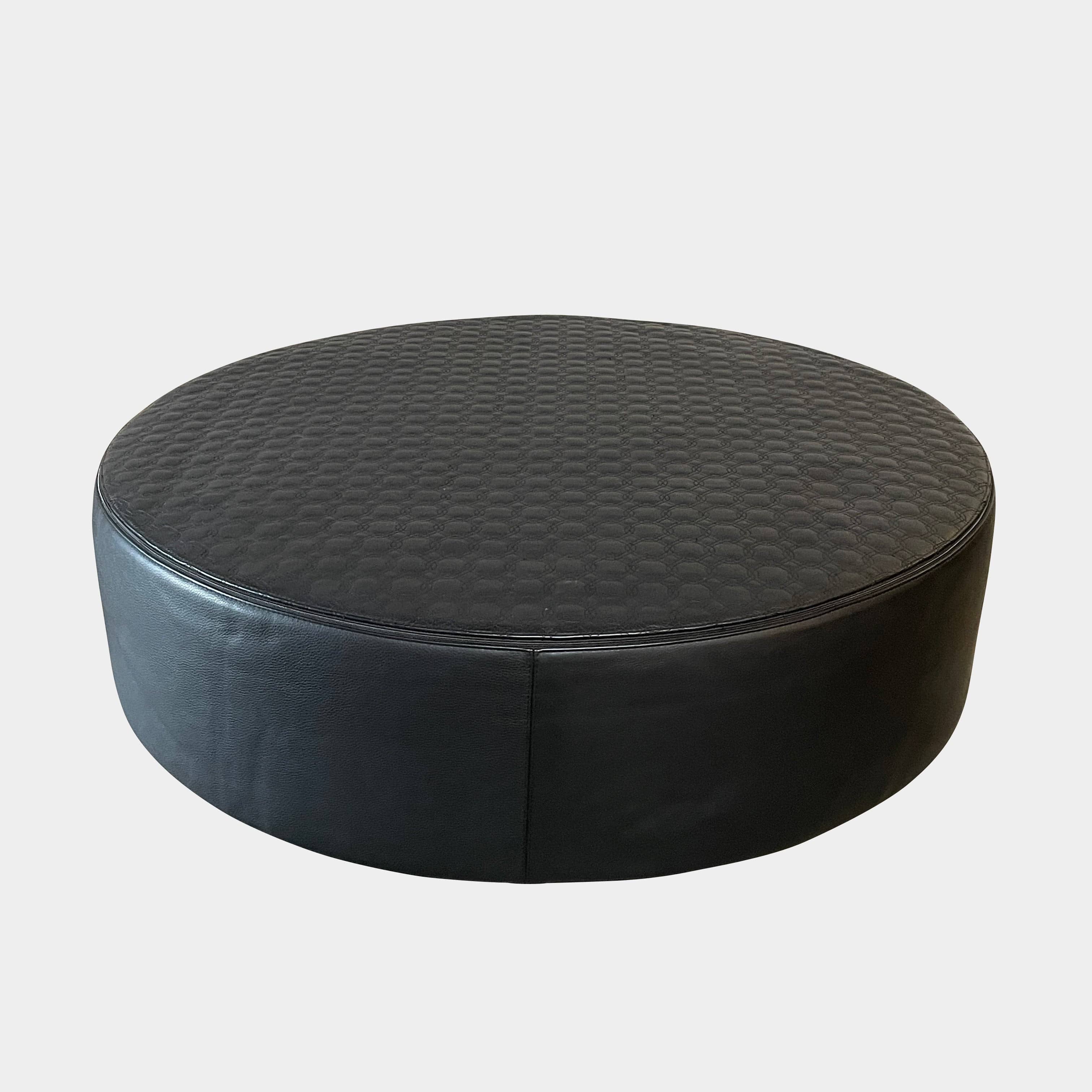 A round black Minotti Yang Leather Ottoman on a white background.
