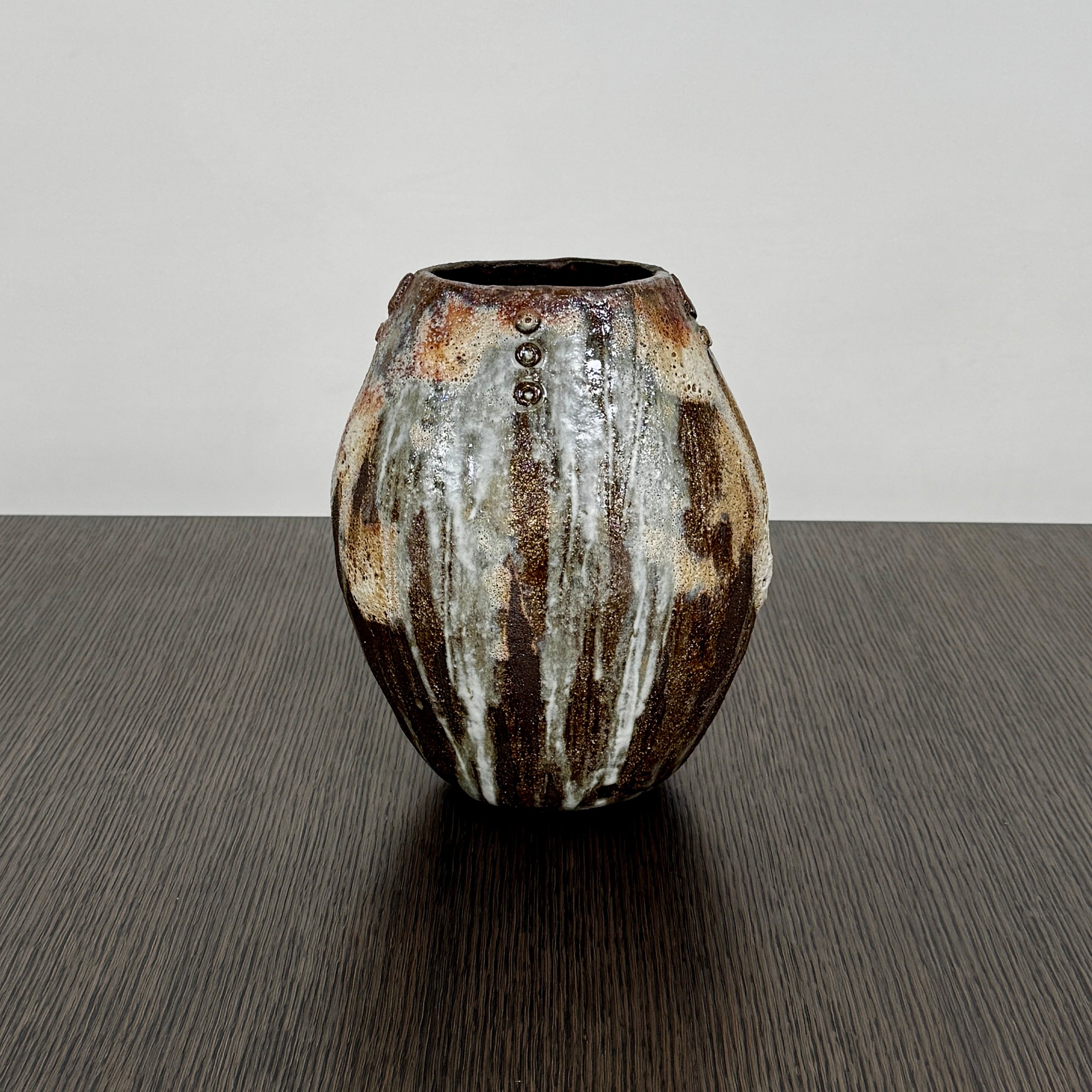 A hand-built dark clay Sofi Ceramics Ocean Vase, Tall by Artist, with irregular brown, black, and white glaze and small circular patterns near the top, set against a plain white background.