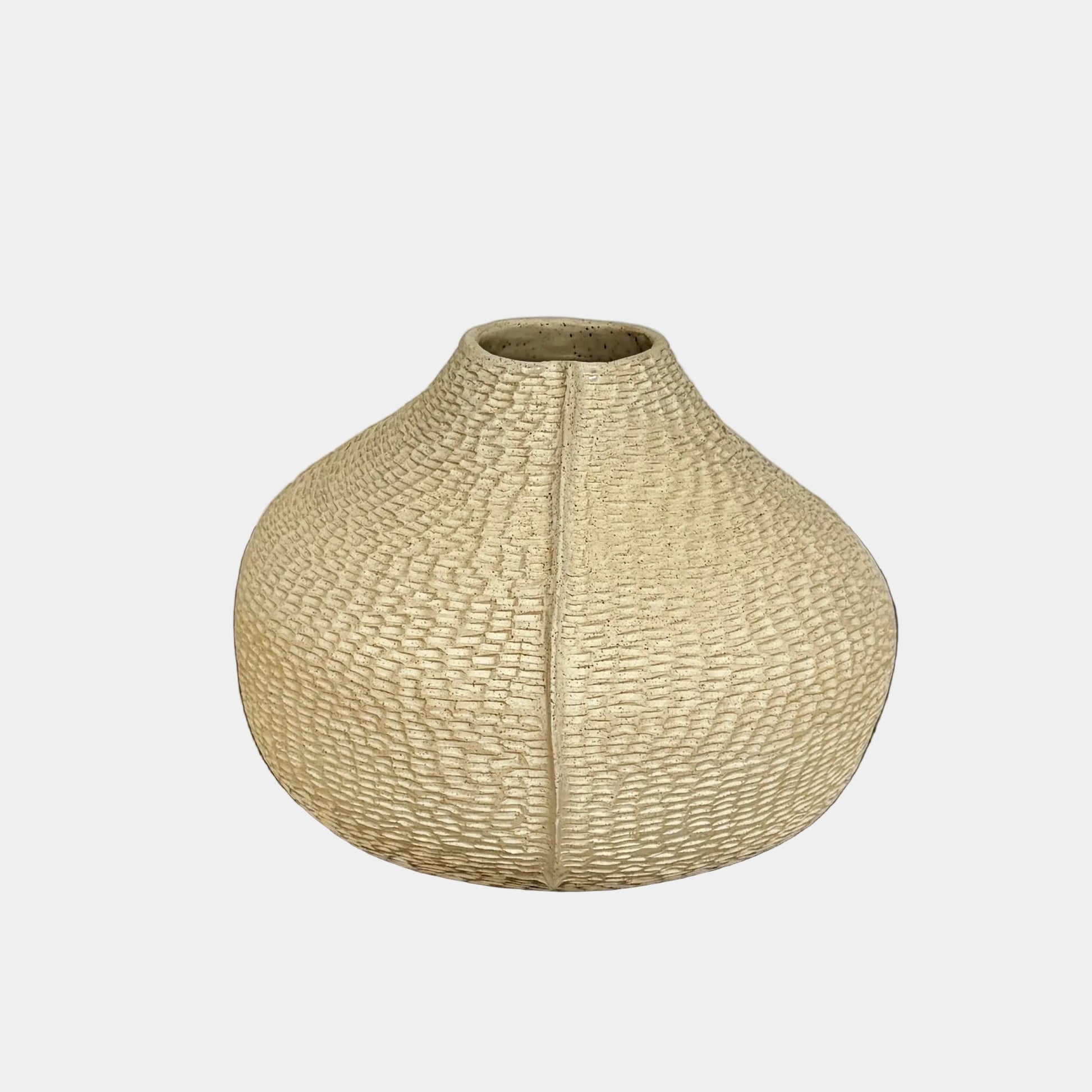 The Sofi Ceramic Pleated Light Clay Vase by Artist, featuring a textured, sculptural form and small opening, sits atop a dark wood-grain surface.