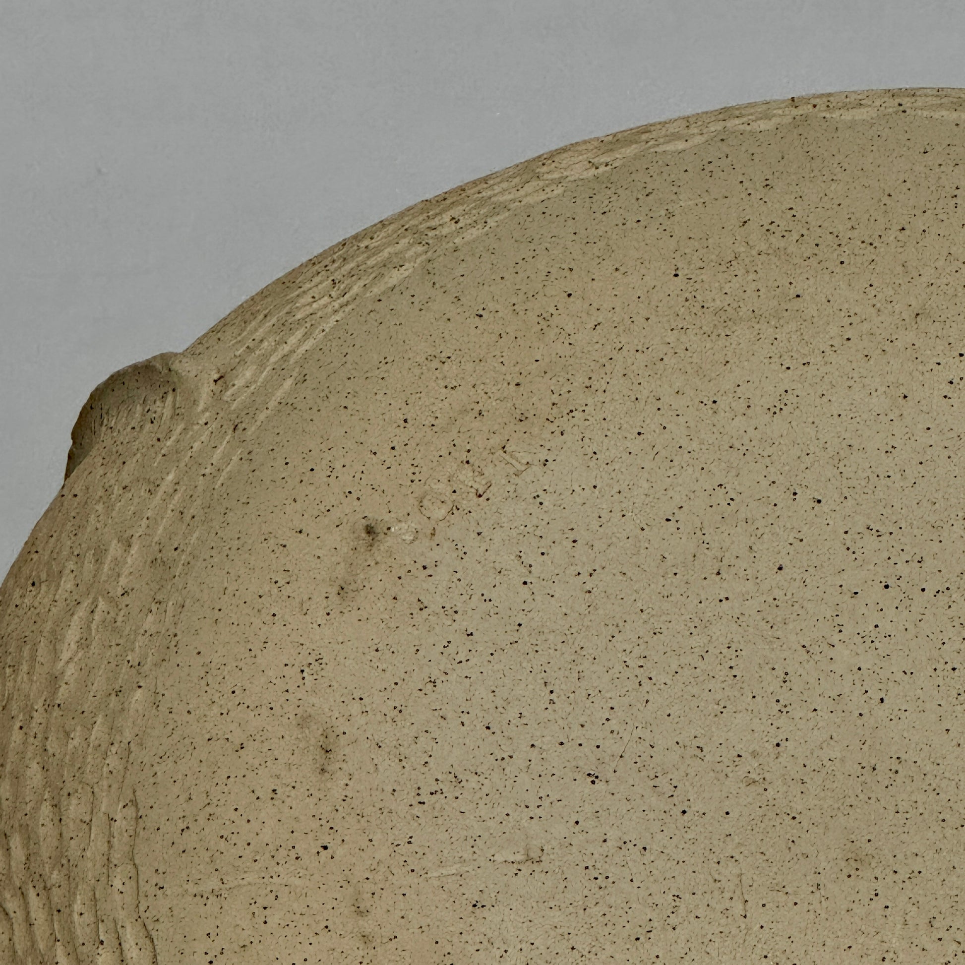 The Sofi Ceramic Pleated Light Clay Vase by Artist, featuring a textured, sculptural form and small opening, sits atop a dark wood-grain surface.