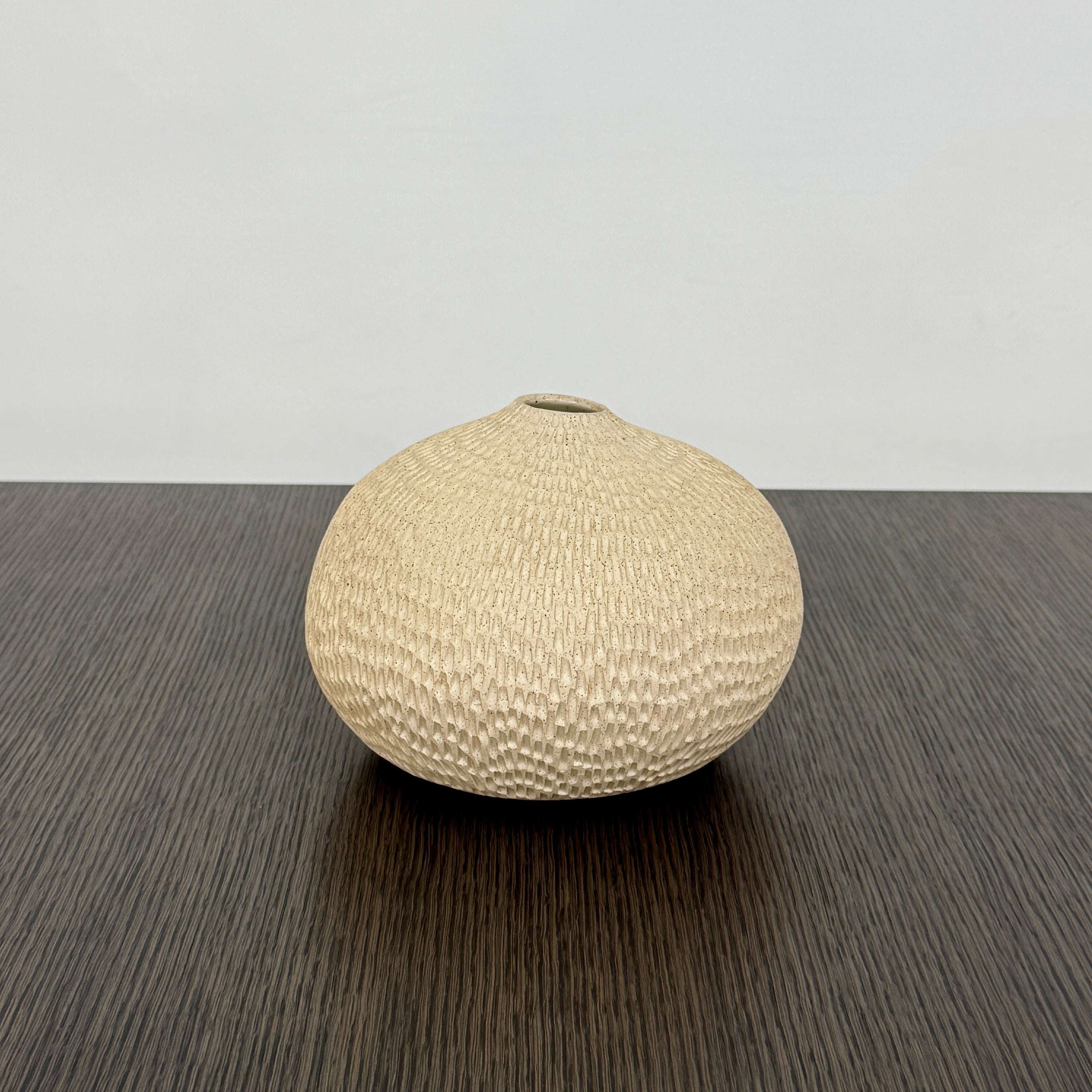 The Artist Sofi Ceramic Pleated Light Clay Vase 2 is a round, beige, textured vessel with a small top opening, shown against a plain white background.