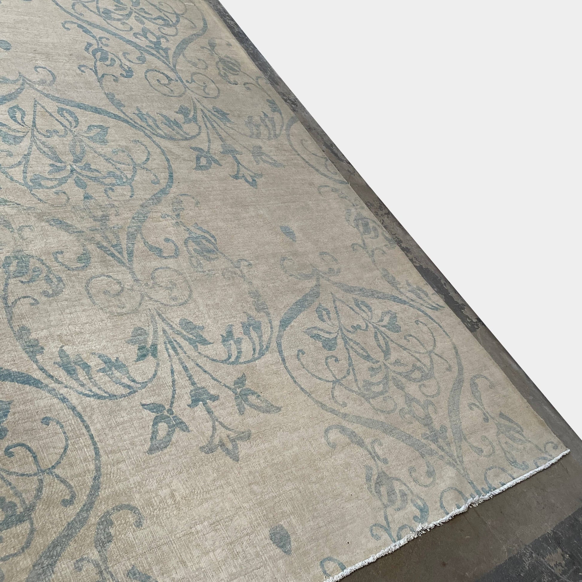 Close-up of a corner of an ornate, traditional Vintage rug with blue patterns on a beige background.