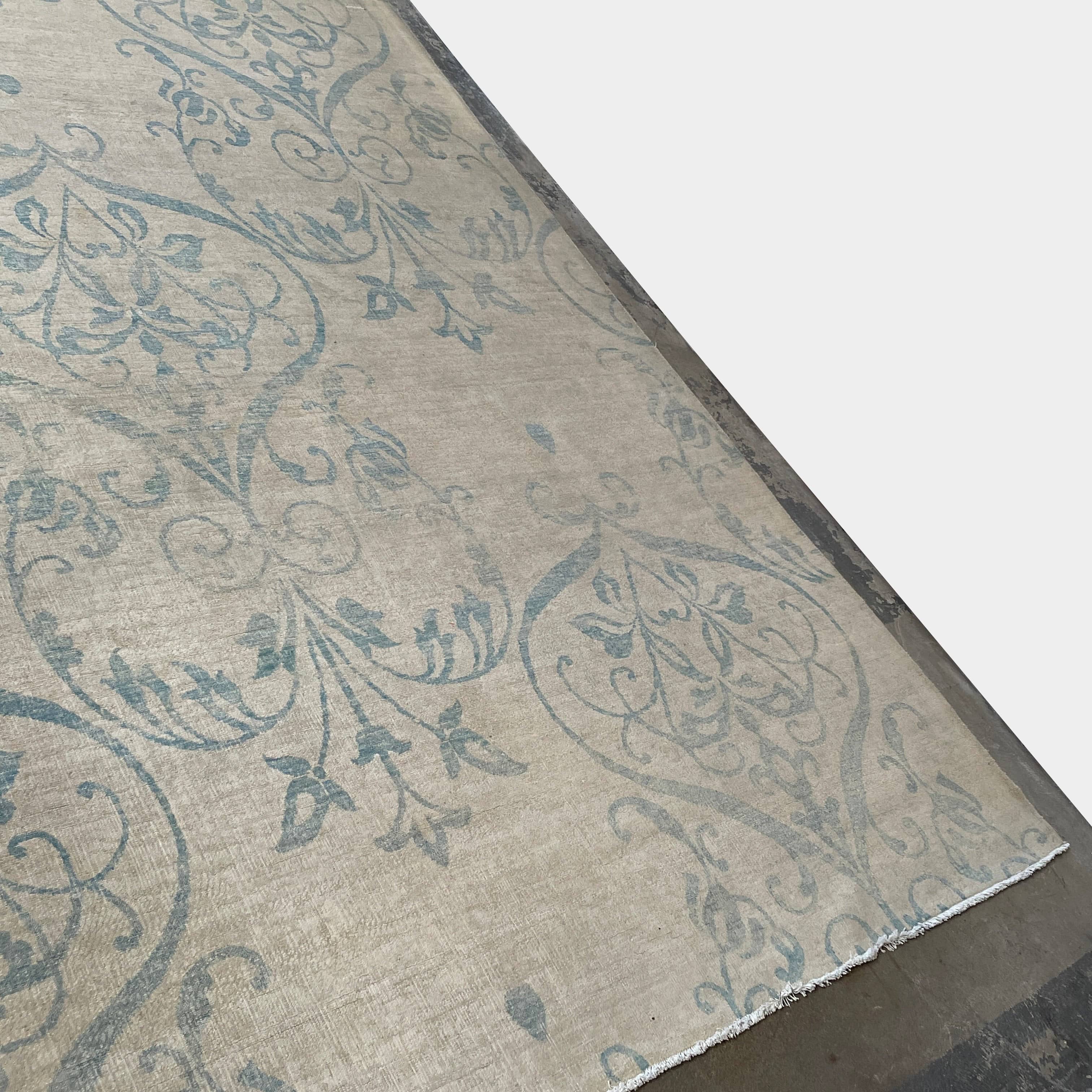 Close-up of a corner of an ornate, traditional Vintage rug with blue patterns on a beige background.