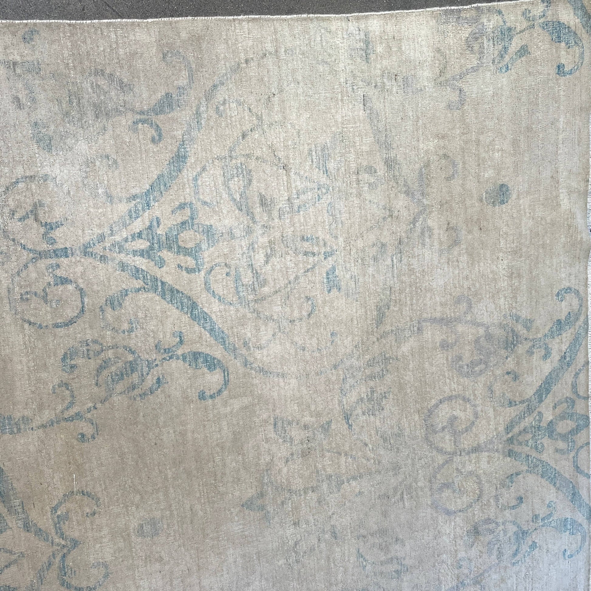 Close-up of a corner of an ornate, traditional Vintage rug with blue patterns on a beige background.