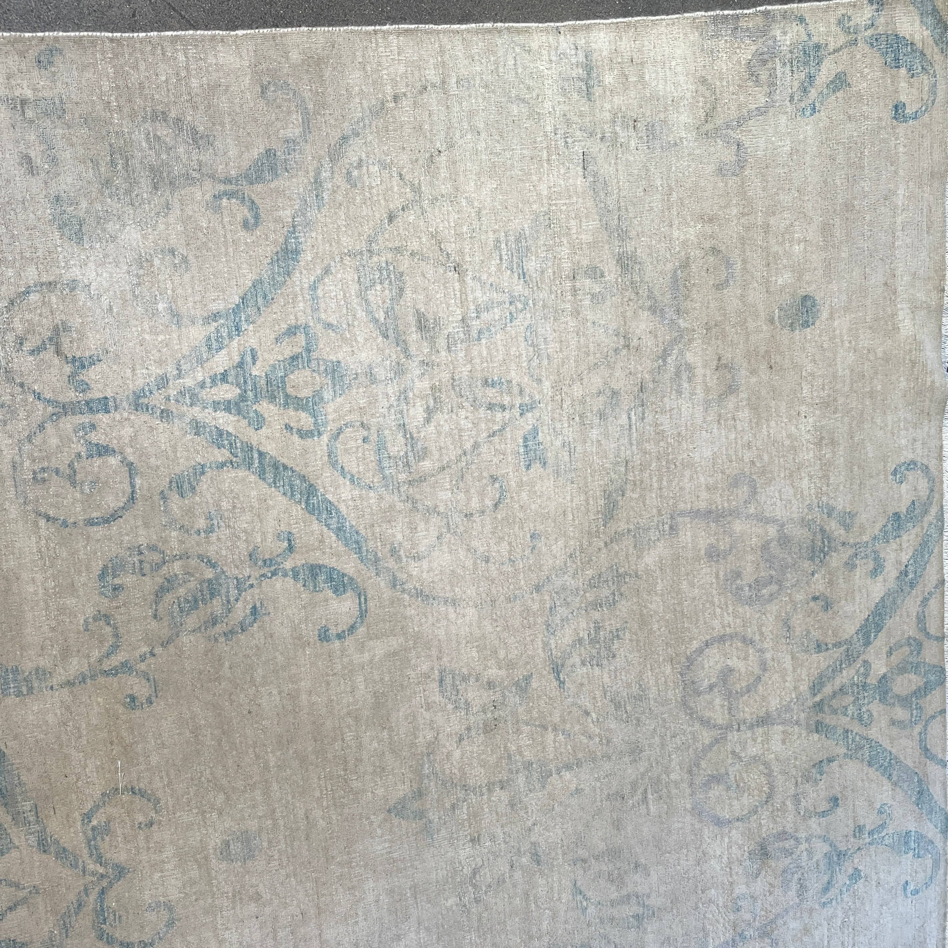 Close-up of a corner of an ornate, traditional Vintage rug with blue patterns on a beige background.